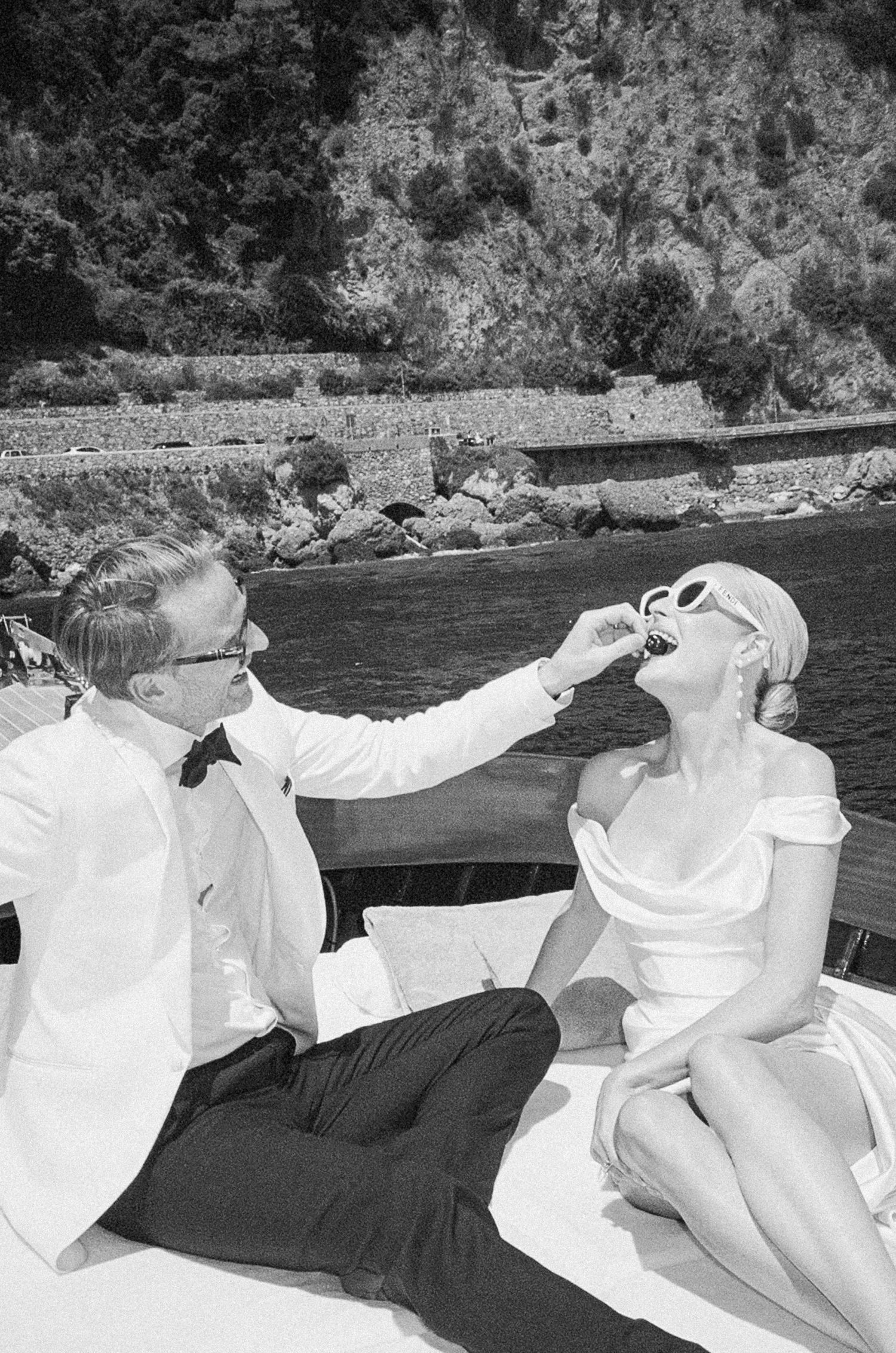 Elegant couple in vintage attire sharing a playful moment on a boat along the Italian Riviera.