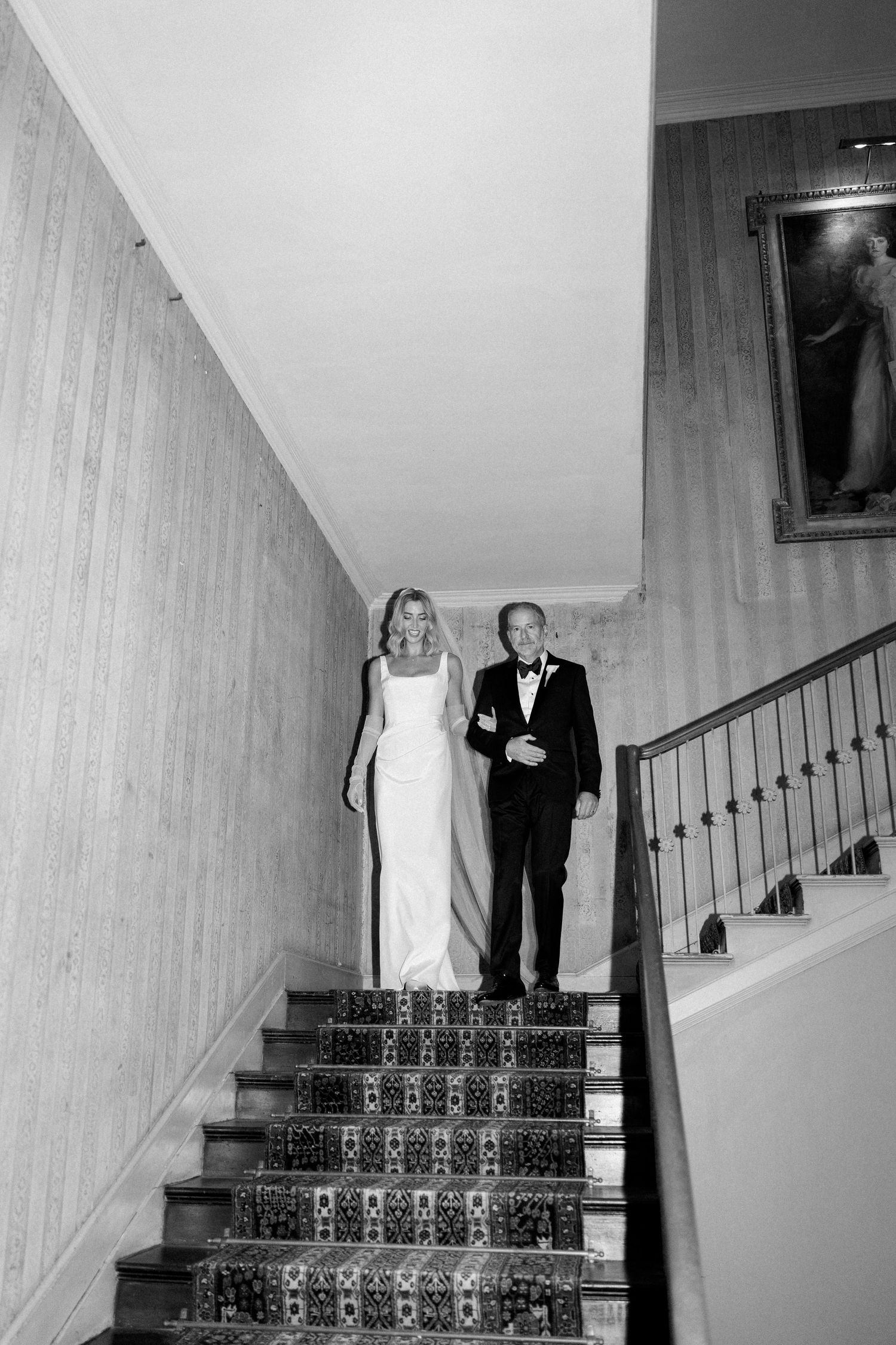 Black and white photo of bride and escort descending ornate tiled staircase.