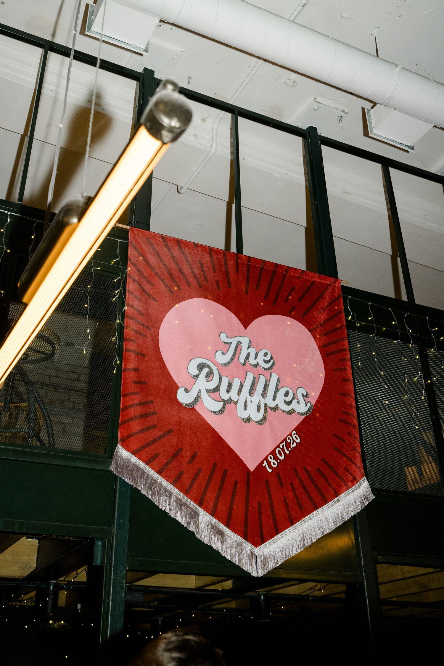 Red heart-shaped wedding banner reading The Ruffles hanging in a decorated reception venue.