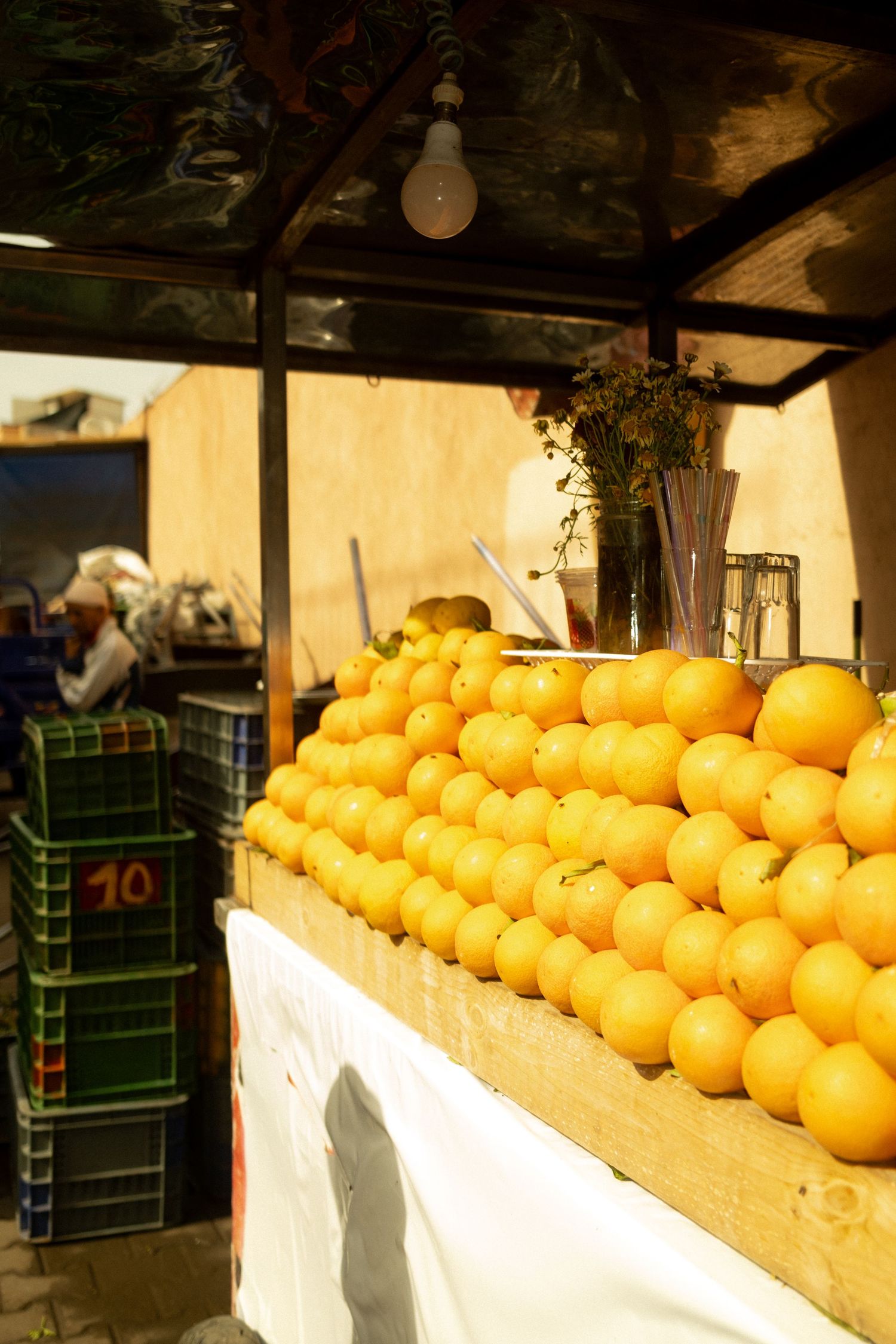 Fresh oranges stacked in a pyramid display at an outdoor market fruit stand with a light bulb overhead.
