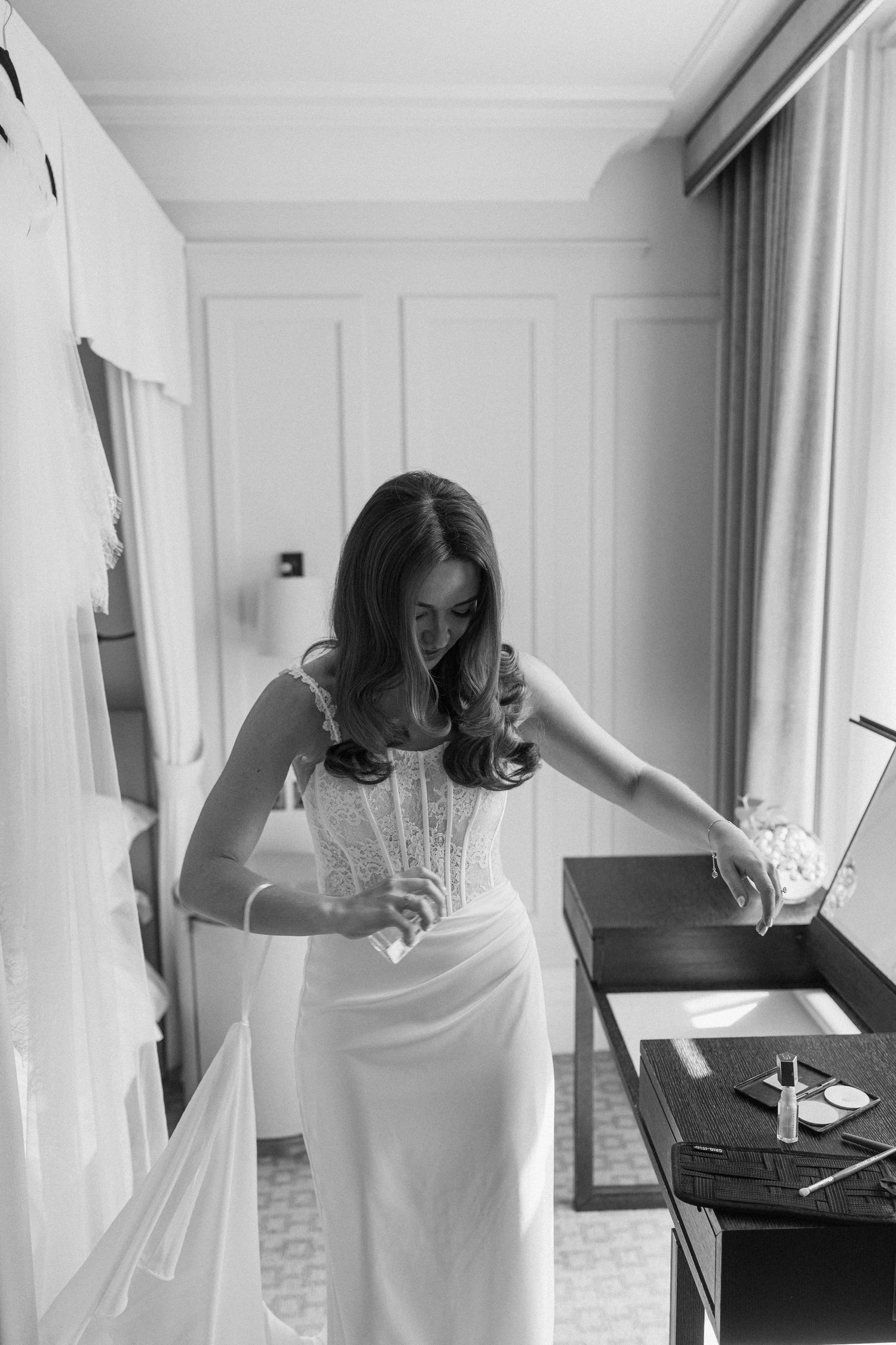 Black and white photo of bride in corset gown spritzing perfume before wedding.