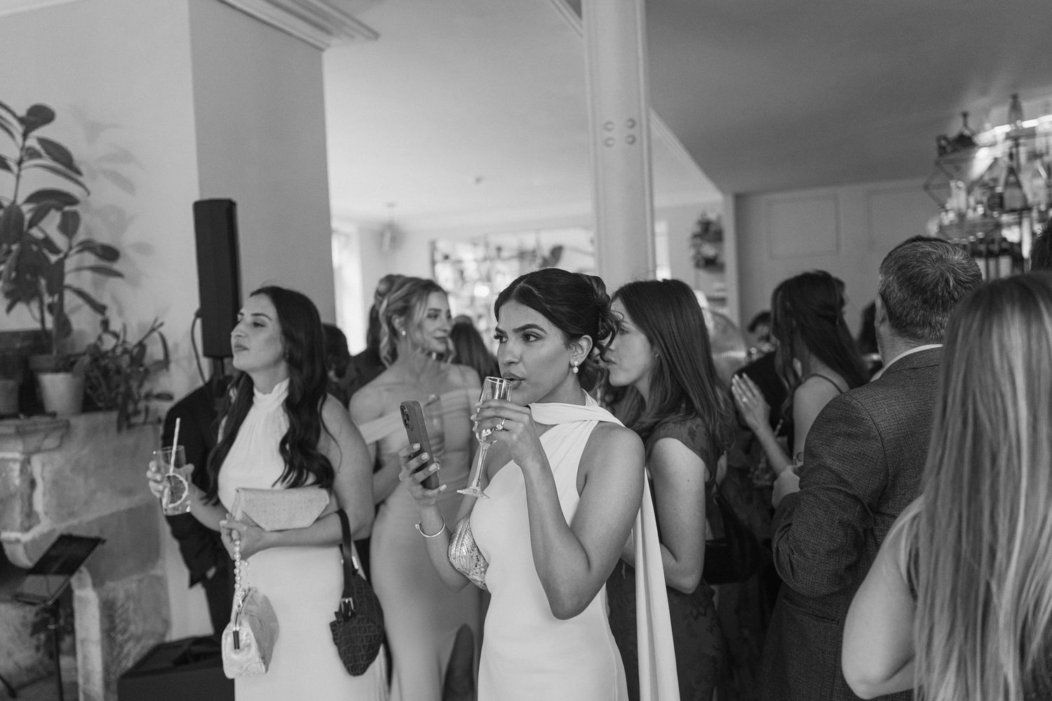 Black and white photo of elegantly dressed wedding guests mingling and celebrating at reception.