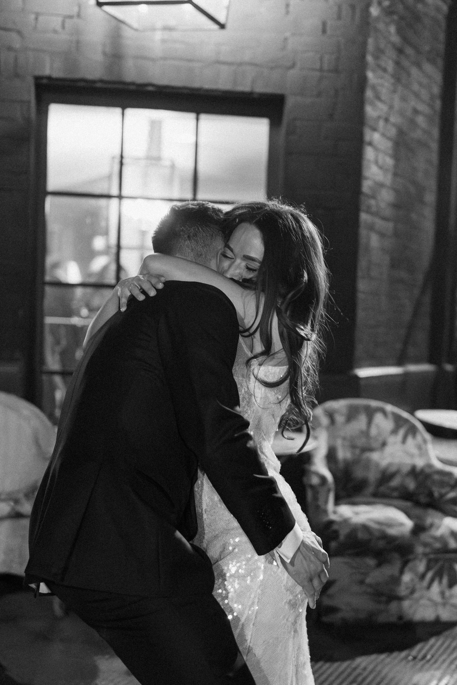 Bride and groom share emotional first dance embrace in black and white wedding reception photo.