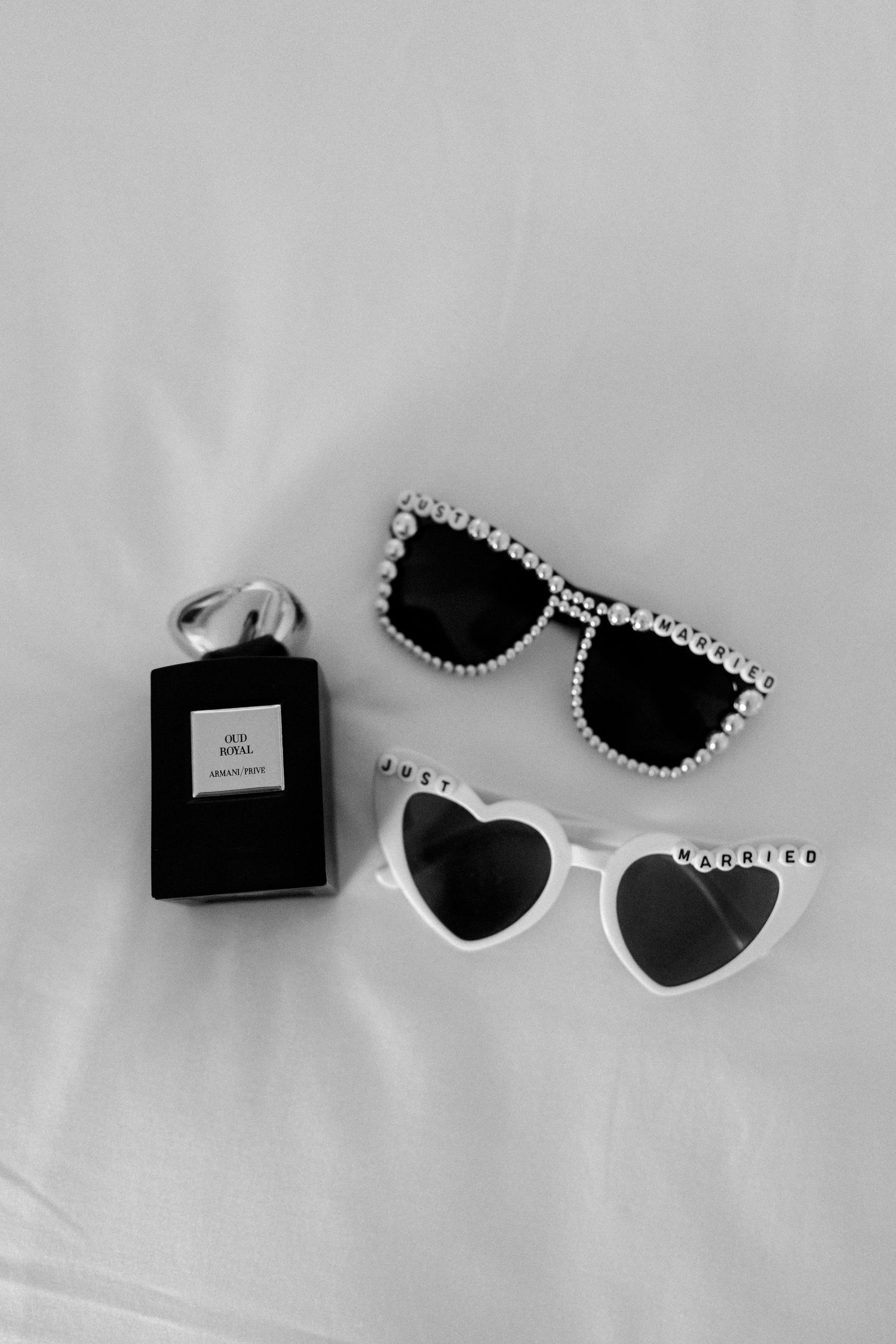 Stylish sunglasses and perfume bottle arranged on white surface in black and white.