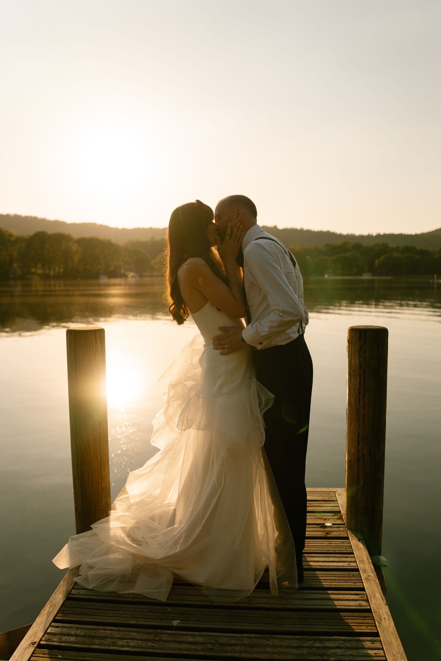 Couple shares intimate moments on a wooden dock during golden hour by a serene lake.