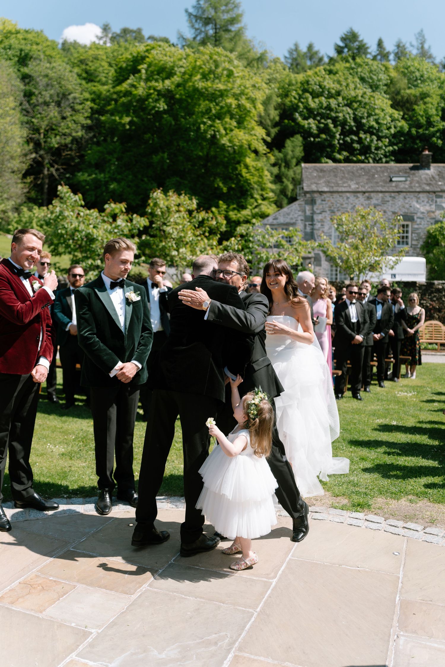 Wedding party lines up on stone pathway during sunny outdoor ceremony.