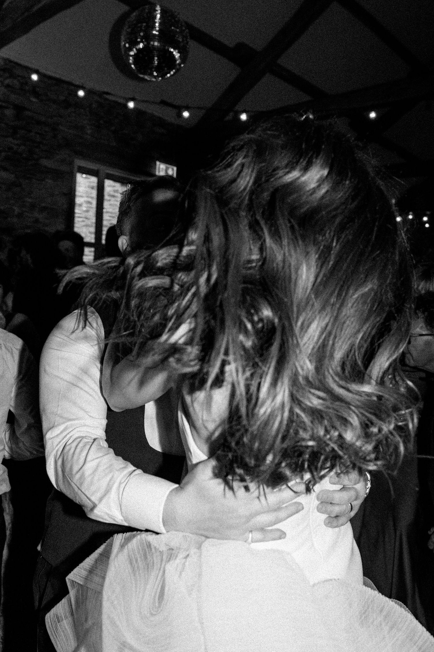Black and white photo of dancing couples at a wedding reception with string lights overhead.
