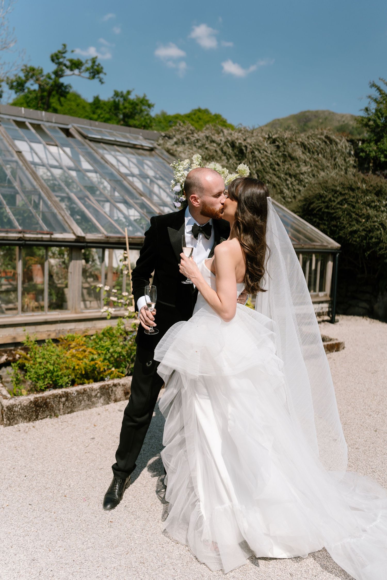A romantic wedding couple shares a kiss in front of a greenhouse on their special day.