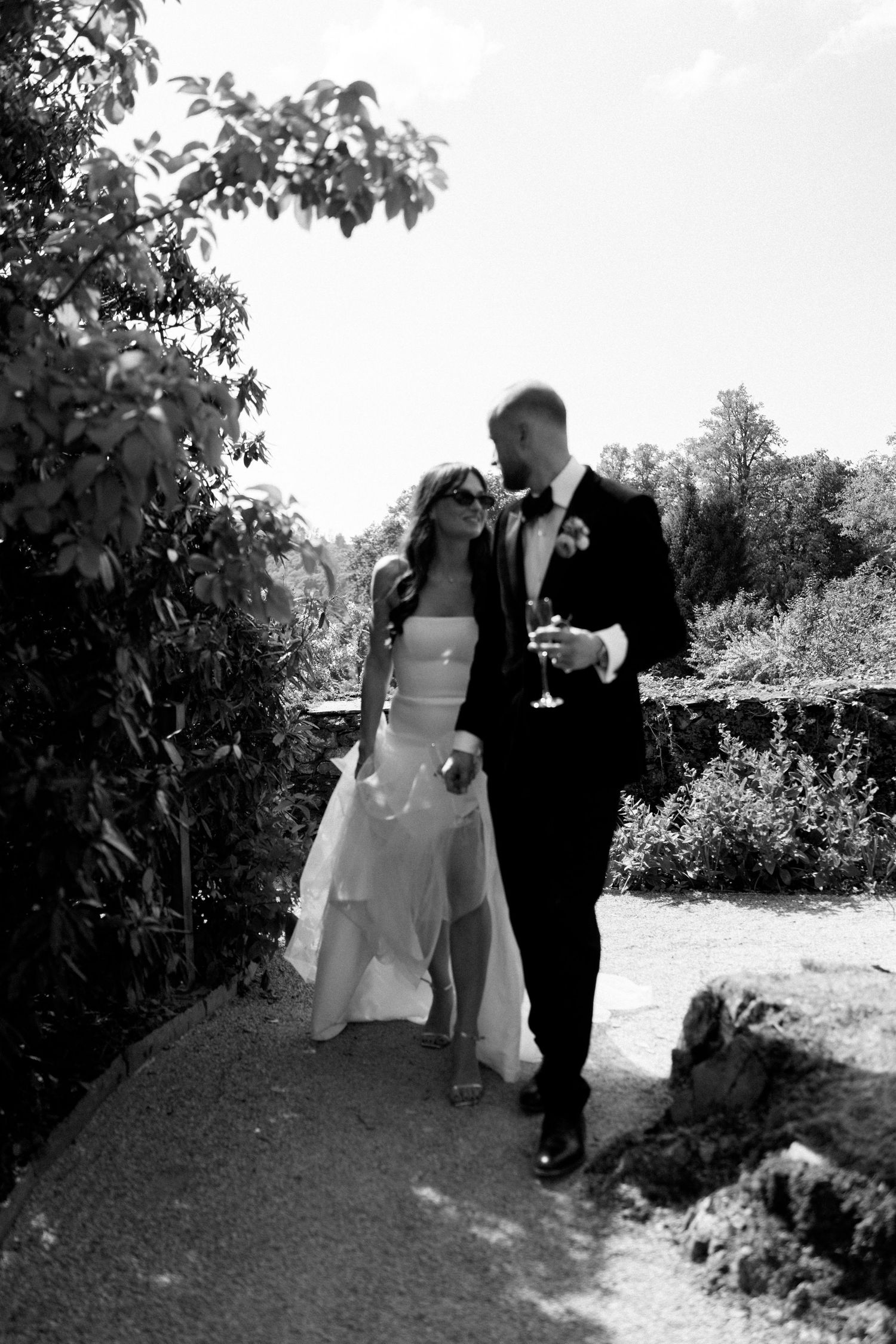 A couple walks together on a garden path during their wedding day photoshoot.