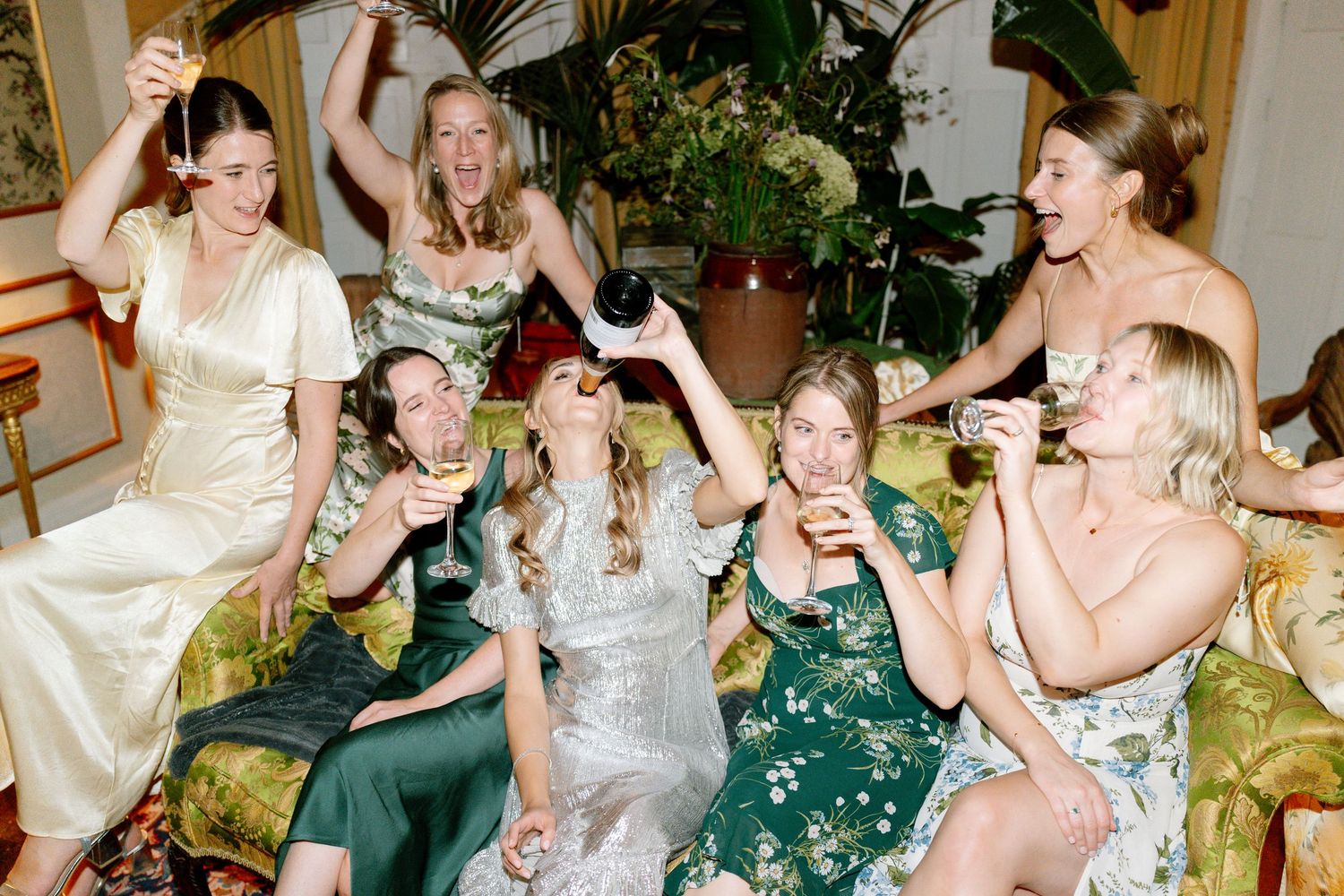 Formal party guests in evening wear seated together on elegant furniture during celebration.