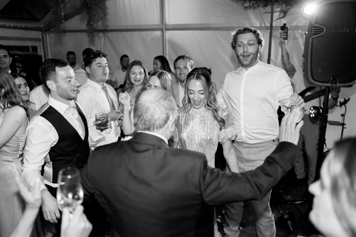 Black and white shot of guests dancing with arms raised at a reception.