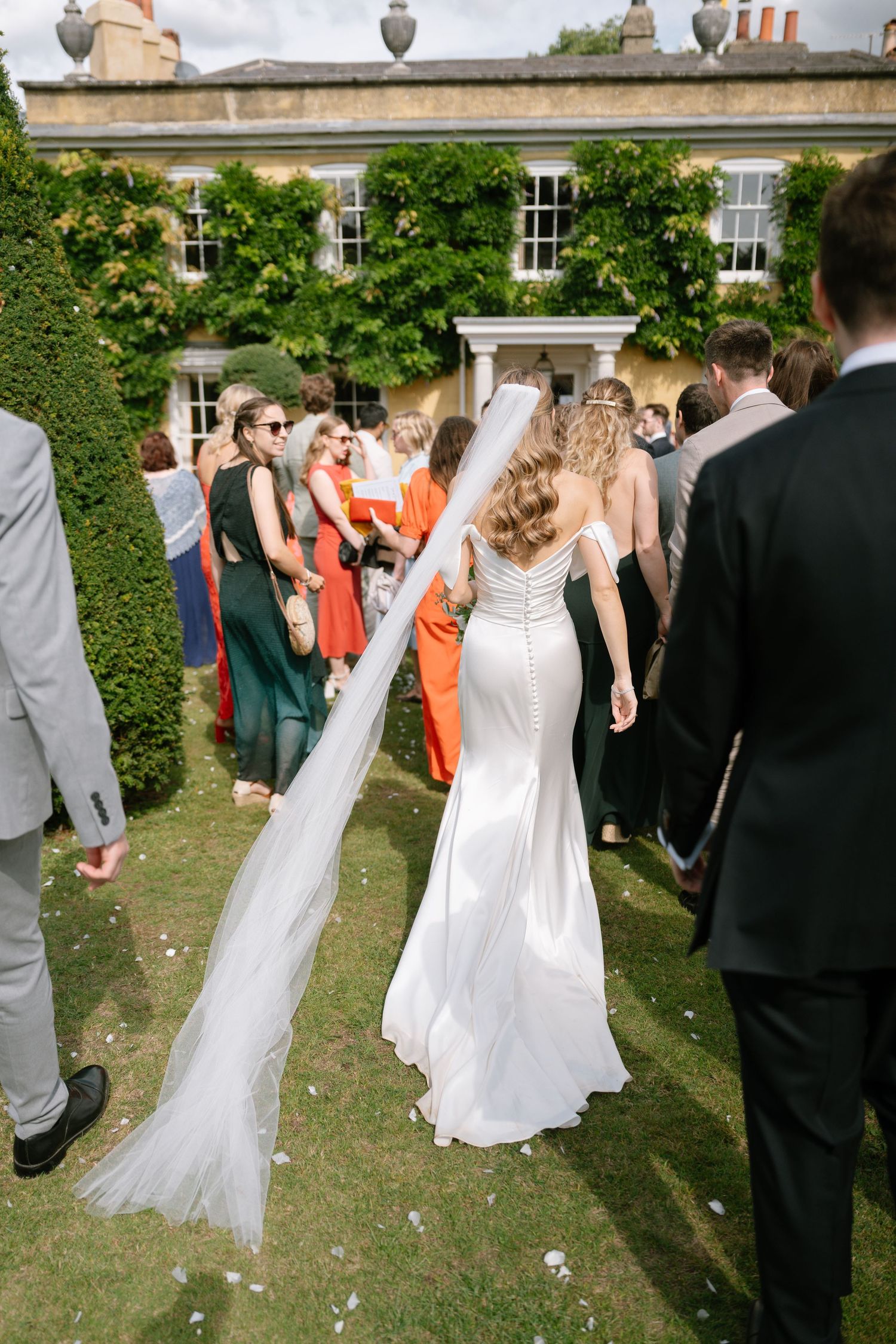 Wedding guests form lines on a lawn while celebrating with the bridal party.