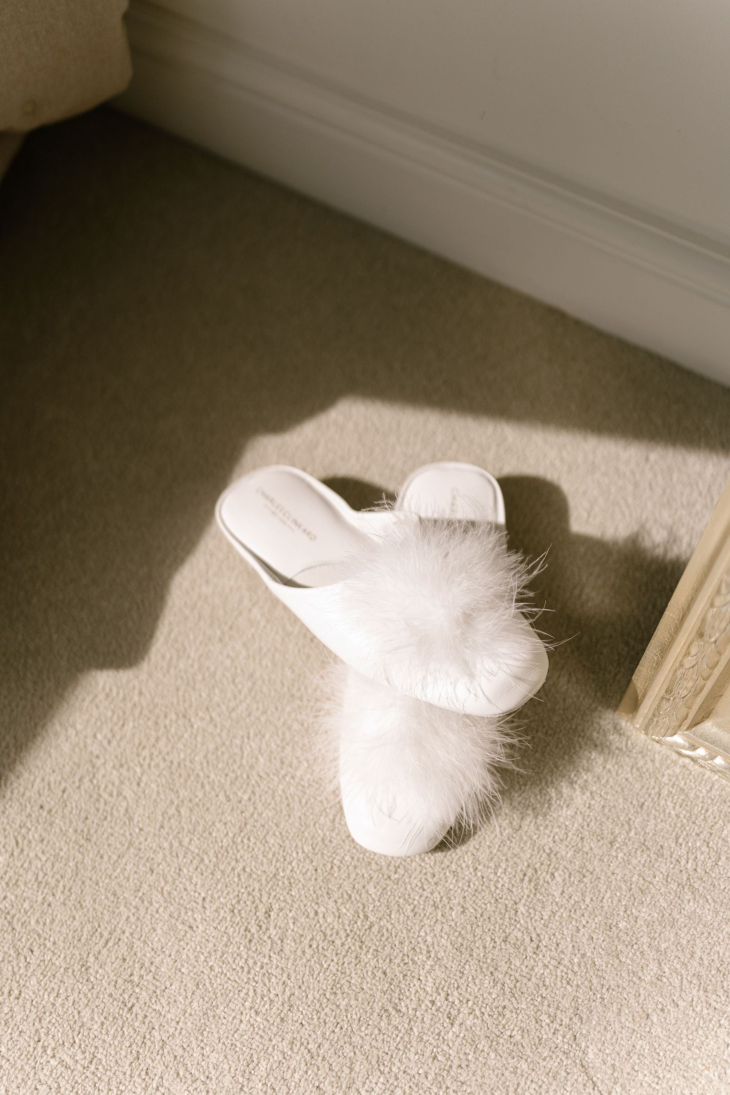 White fluffy slippers arranged in a row on beige carpet with dramatic lighting.