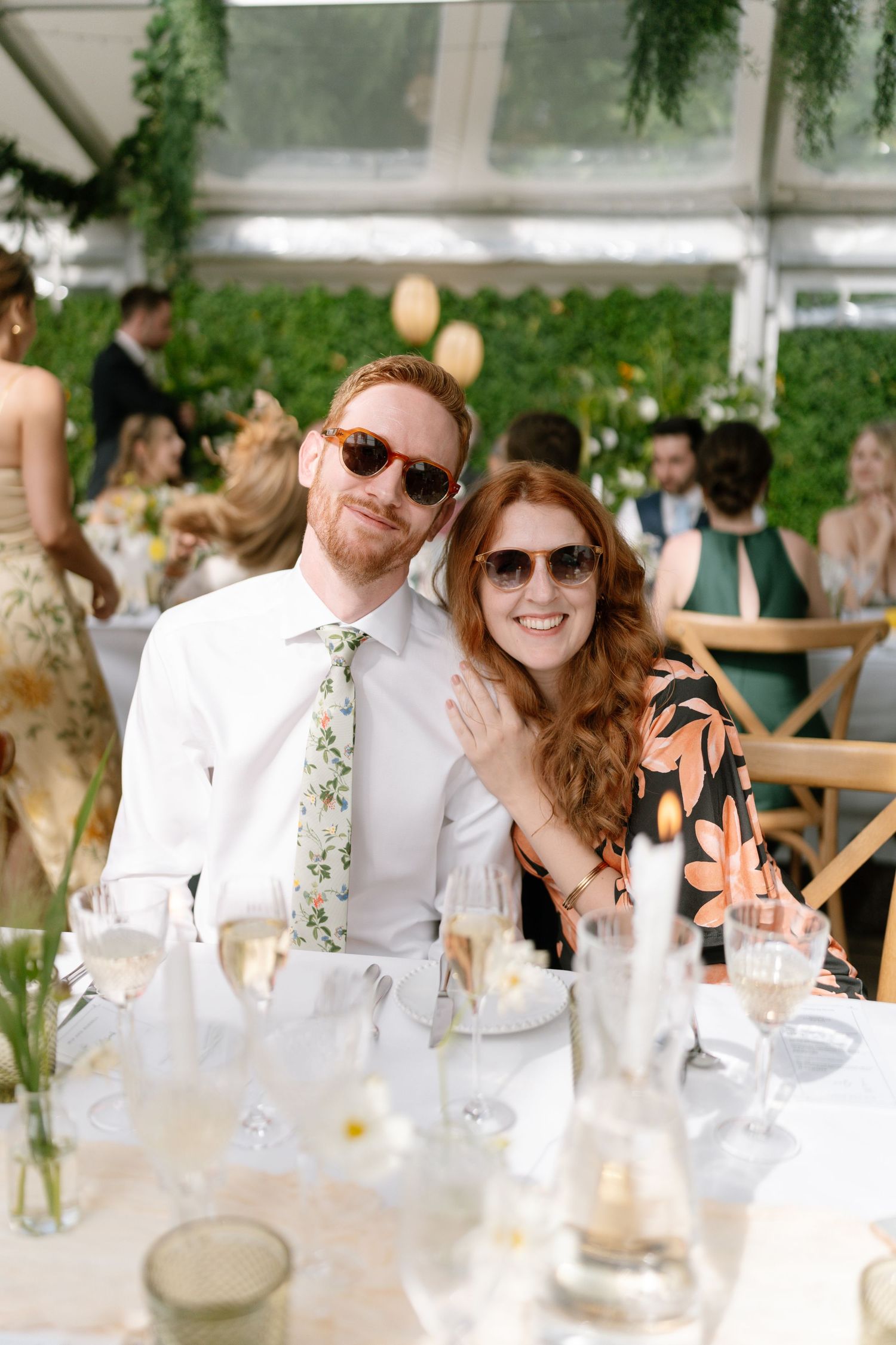 Wedding guests enjoying themselves at a sunny outdoor reception with floral decorations.