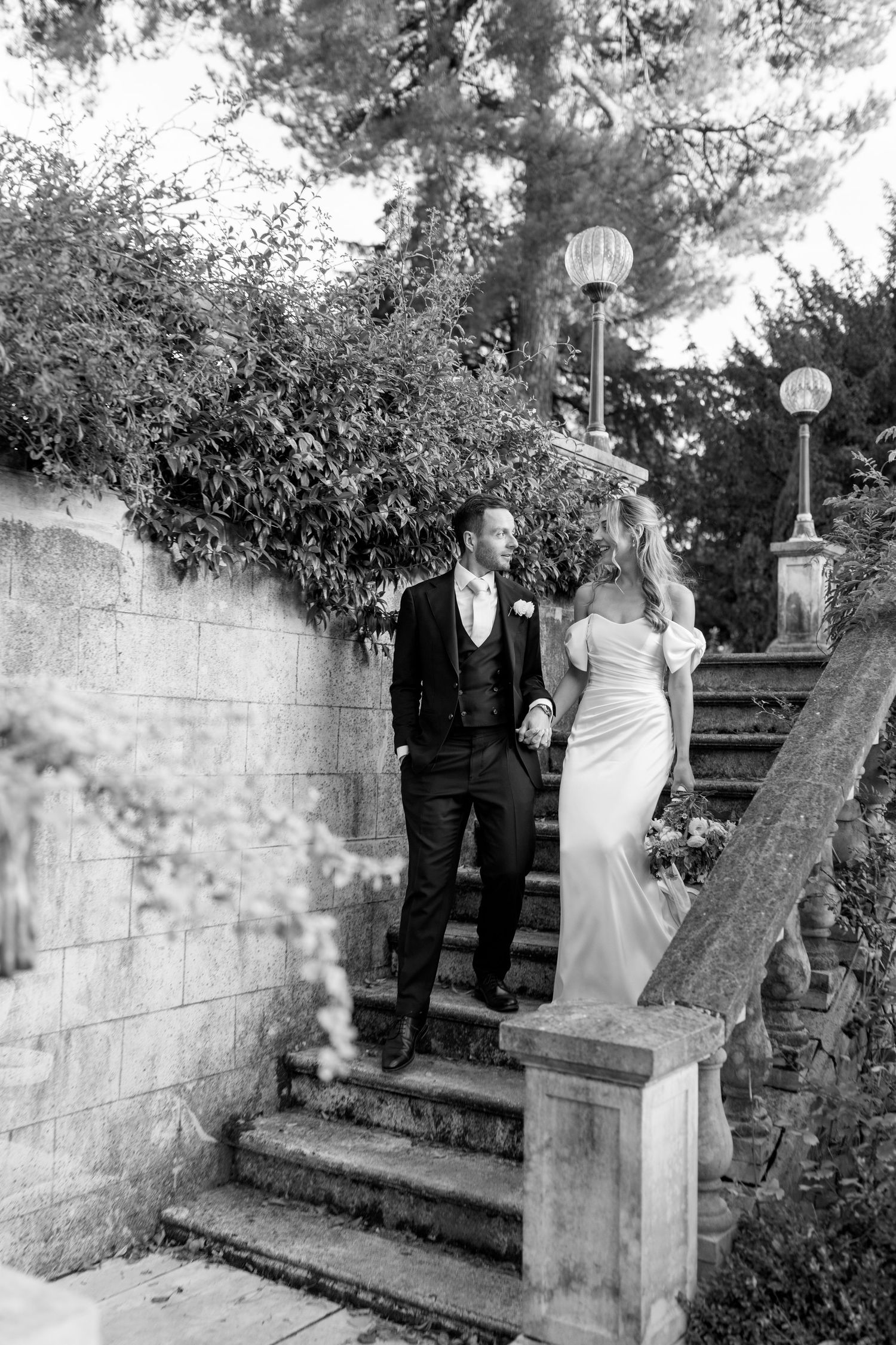 Black and white photo of couple walking up stone garden steps surrounded by foliage.