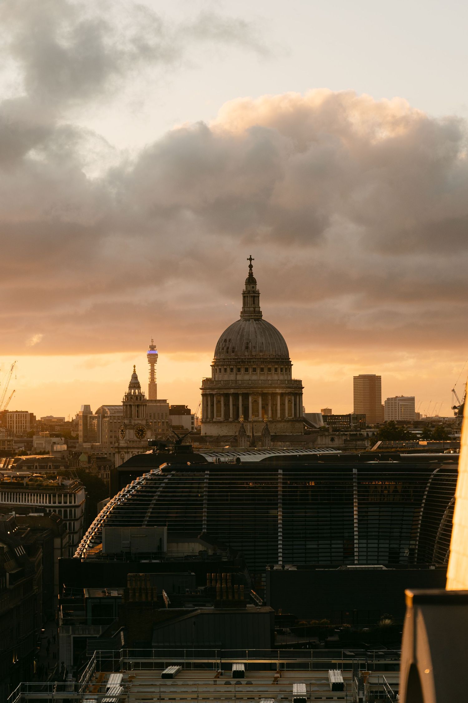 London cityscape at sunset with St Paul's Cathedral dome silhouetted against orange sky.
