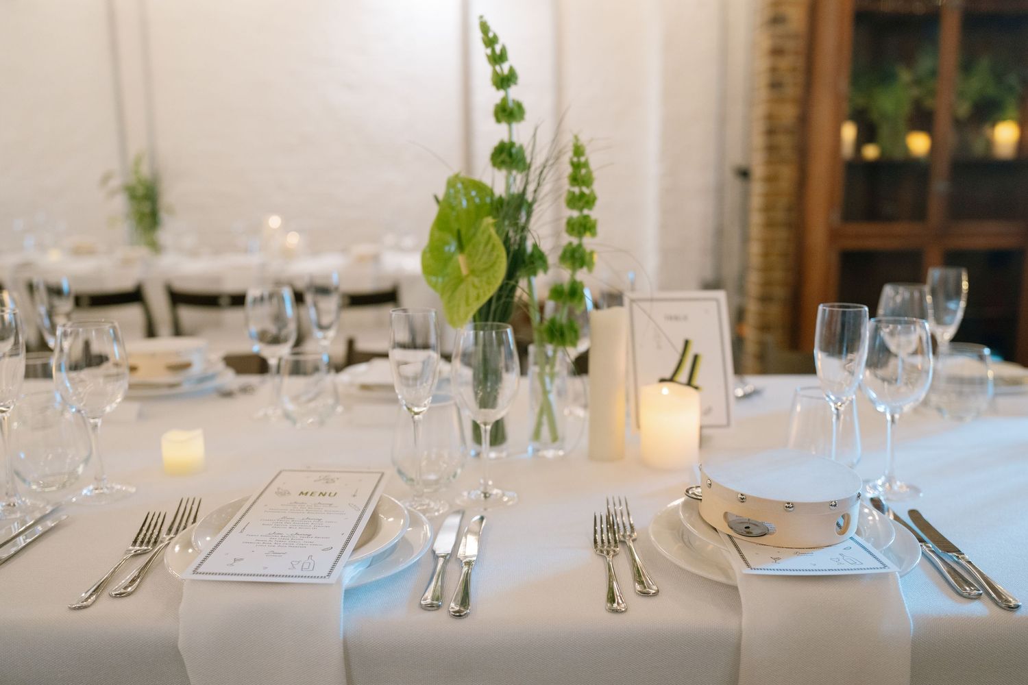 Elegant table settings with white linens, glassware and simple green floral centerpieces.