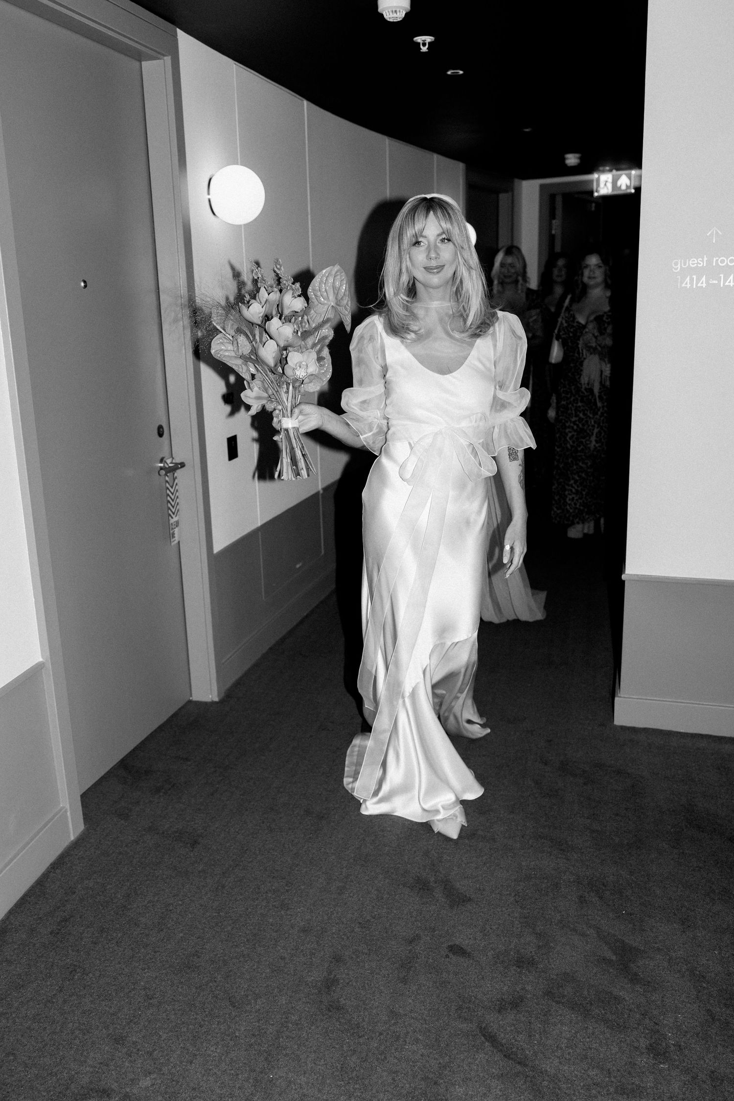 Elegant figure walking down hallway in flowing white silk wedding gown.