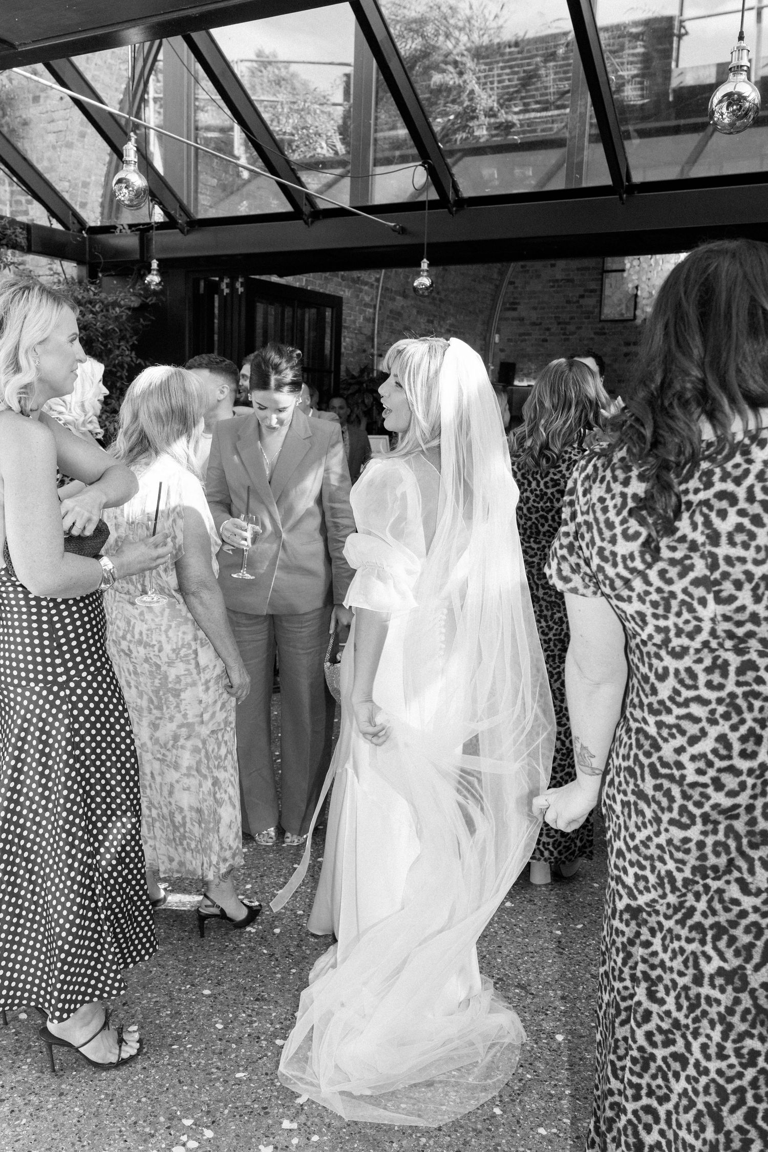 Wedding guests in polka dot dresses and formal attire mingle outdoors during a celebration.