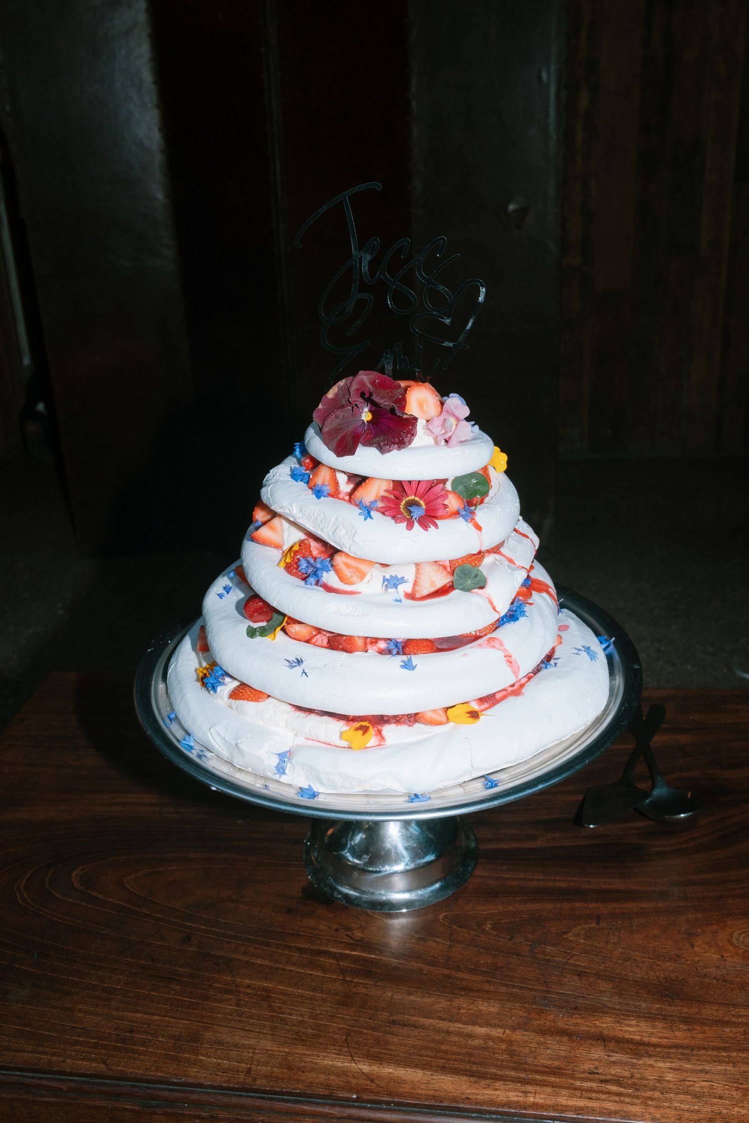 A white tiered wedding cake decorated with colorful flowers sits on a wooden table.