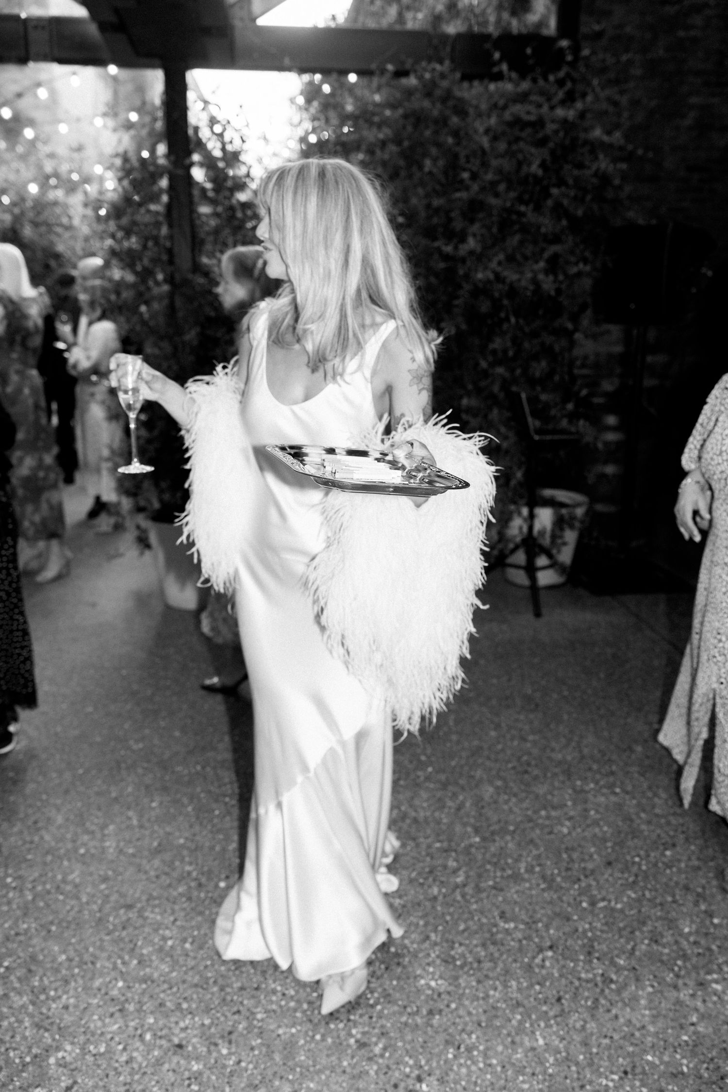 Black and white photos of a bride in a feathered dress dancing at an outdoor reception.