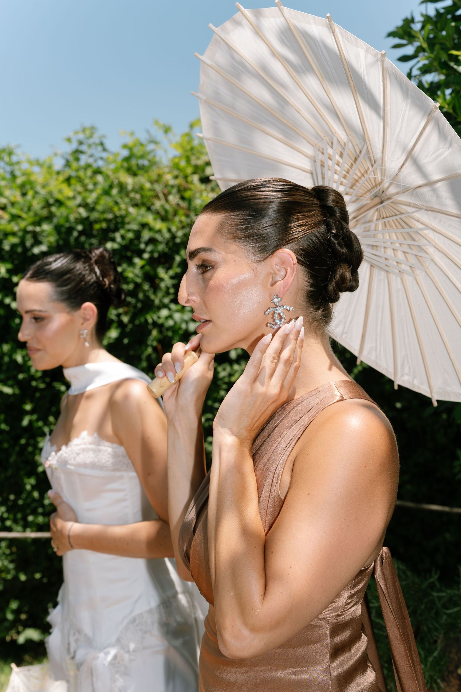 Two elegantly dressed women at an outdoor event, one holding a white parasol and wearing a champagne gown.