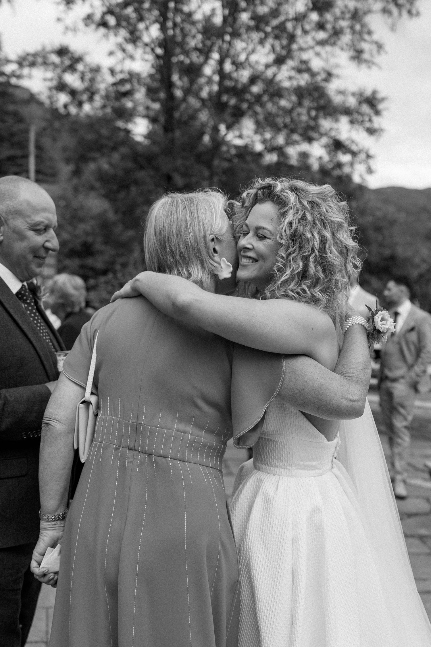 Black and white photo series showing emotional embraces at outdoor wedding celebration.