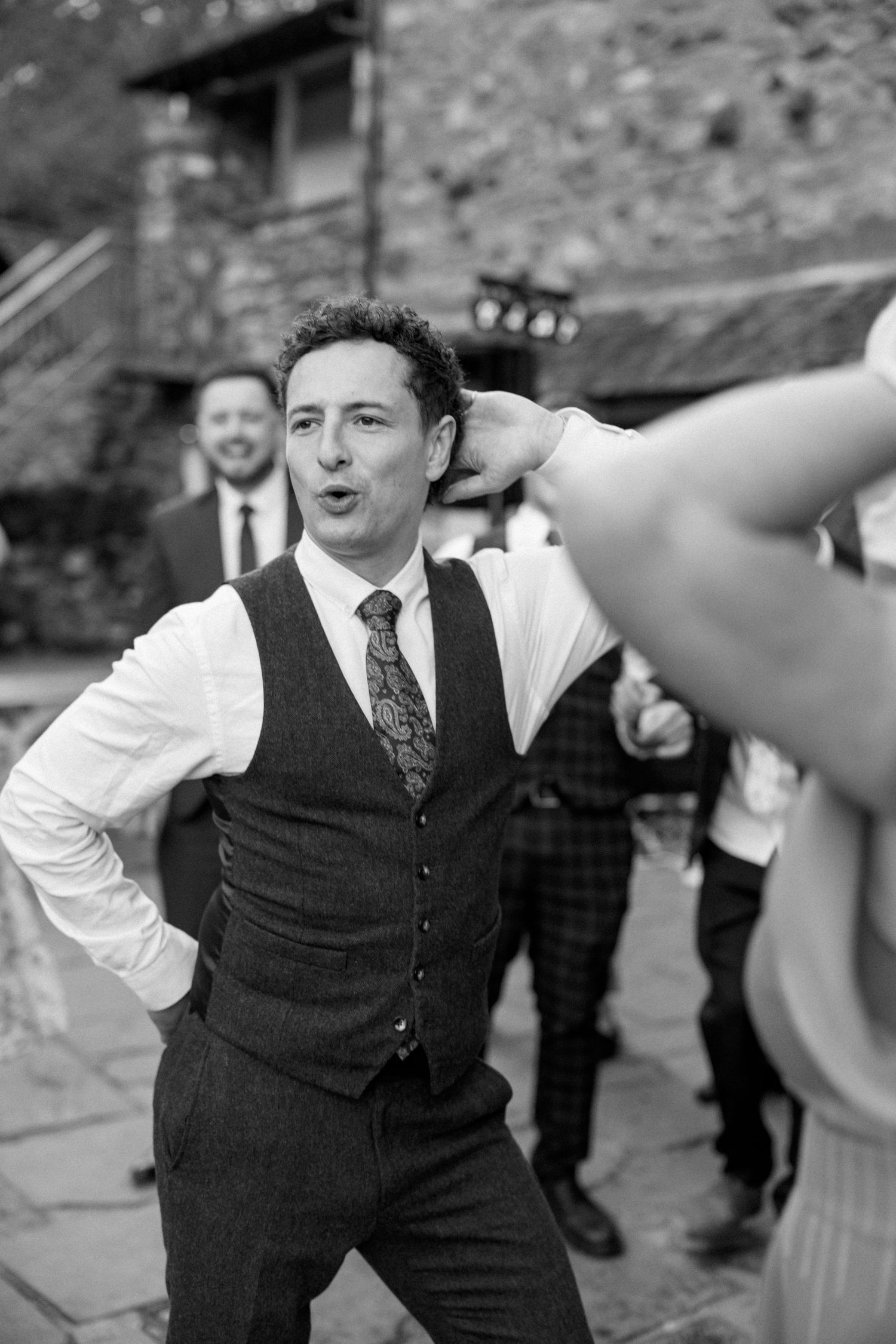 Person in formal vest and tie dancing energetically at outdoor event.