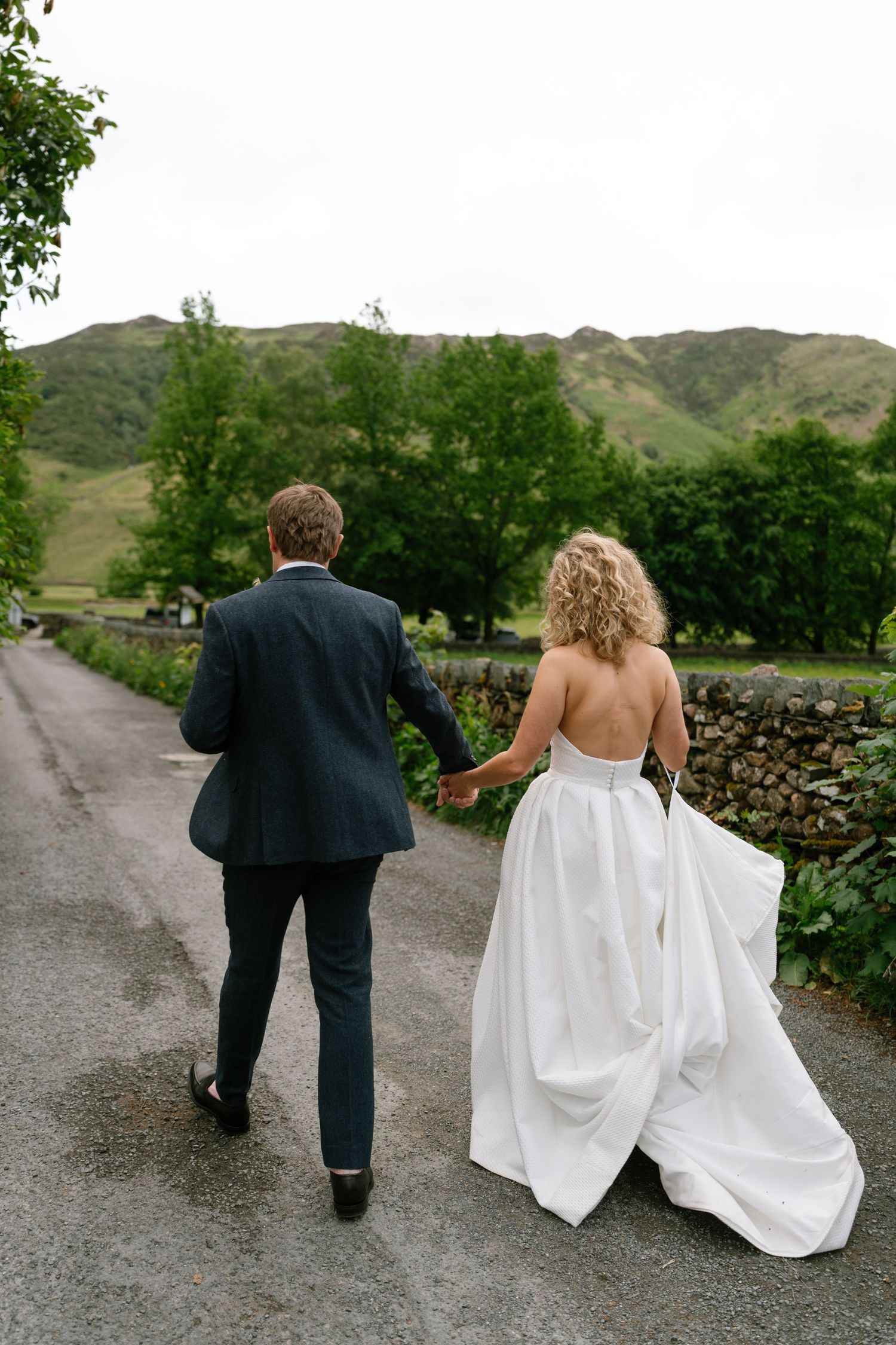 Couple walking down country road with green hills in background.