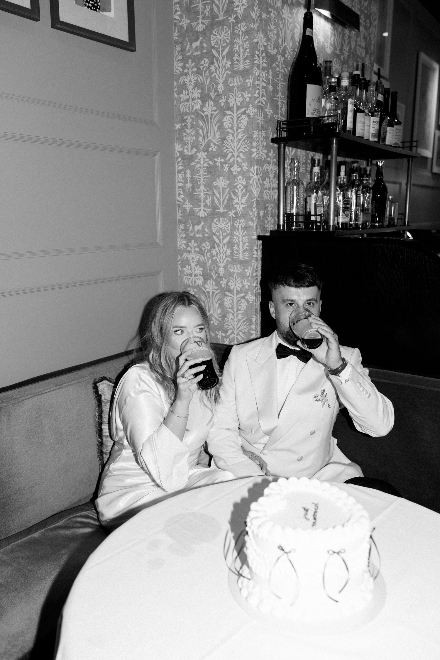Couple in formal attire relaxing on white furniture at an elegant venue.