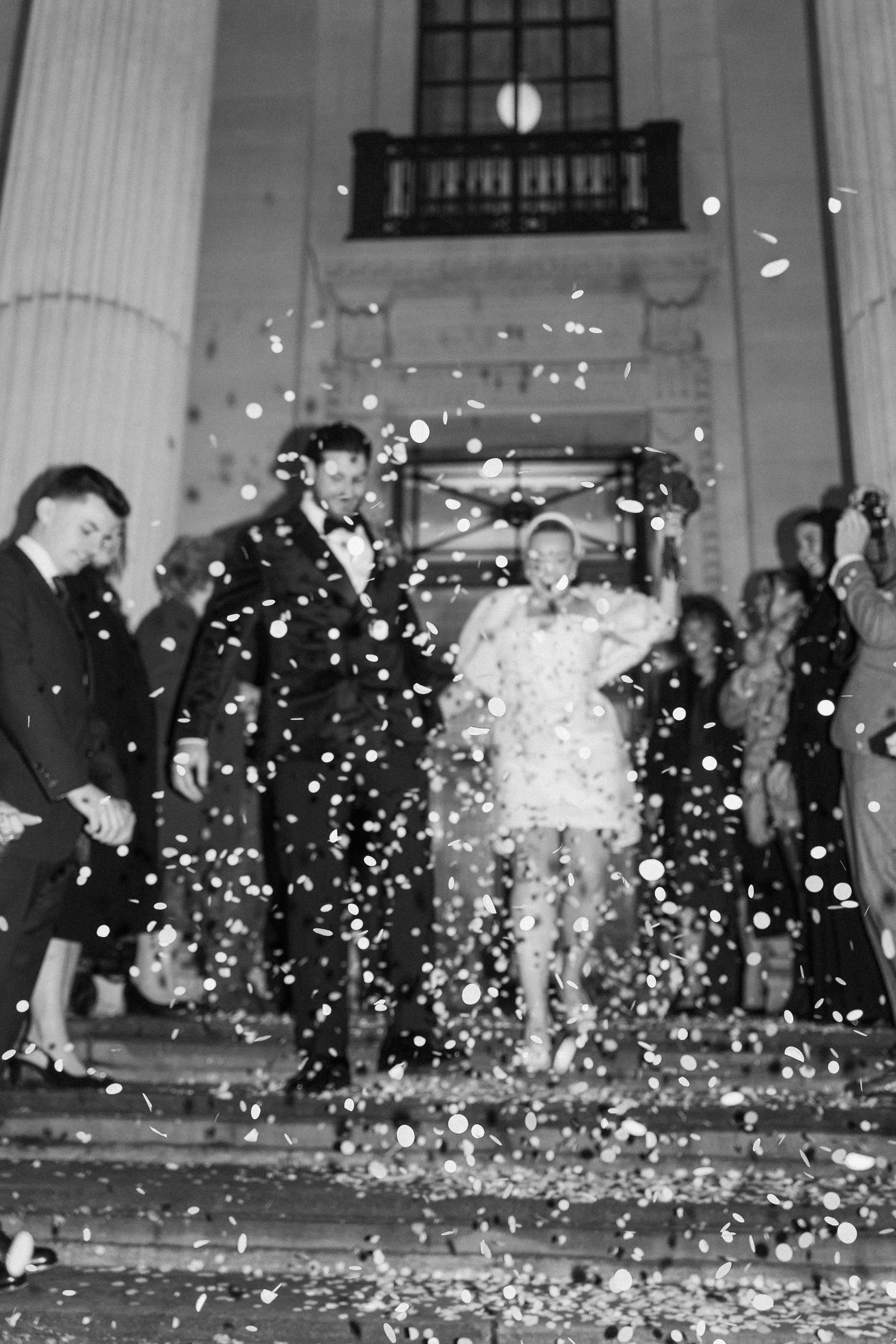 Wedding celebration with confetti falling on steps of a classical building.