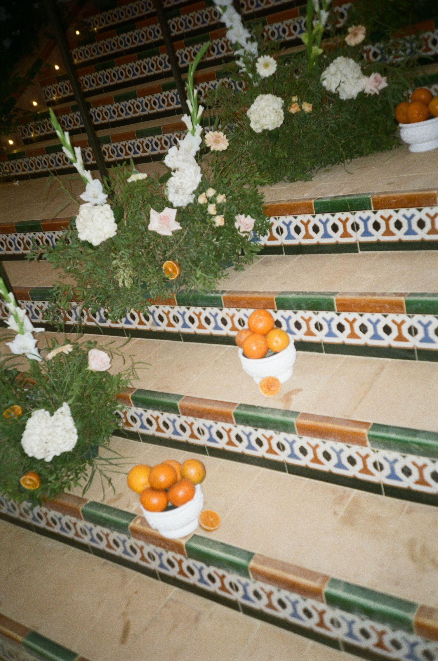 White floral arrangements and oranges decorate a curved tiled bench in an outdoor setting.