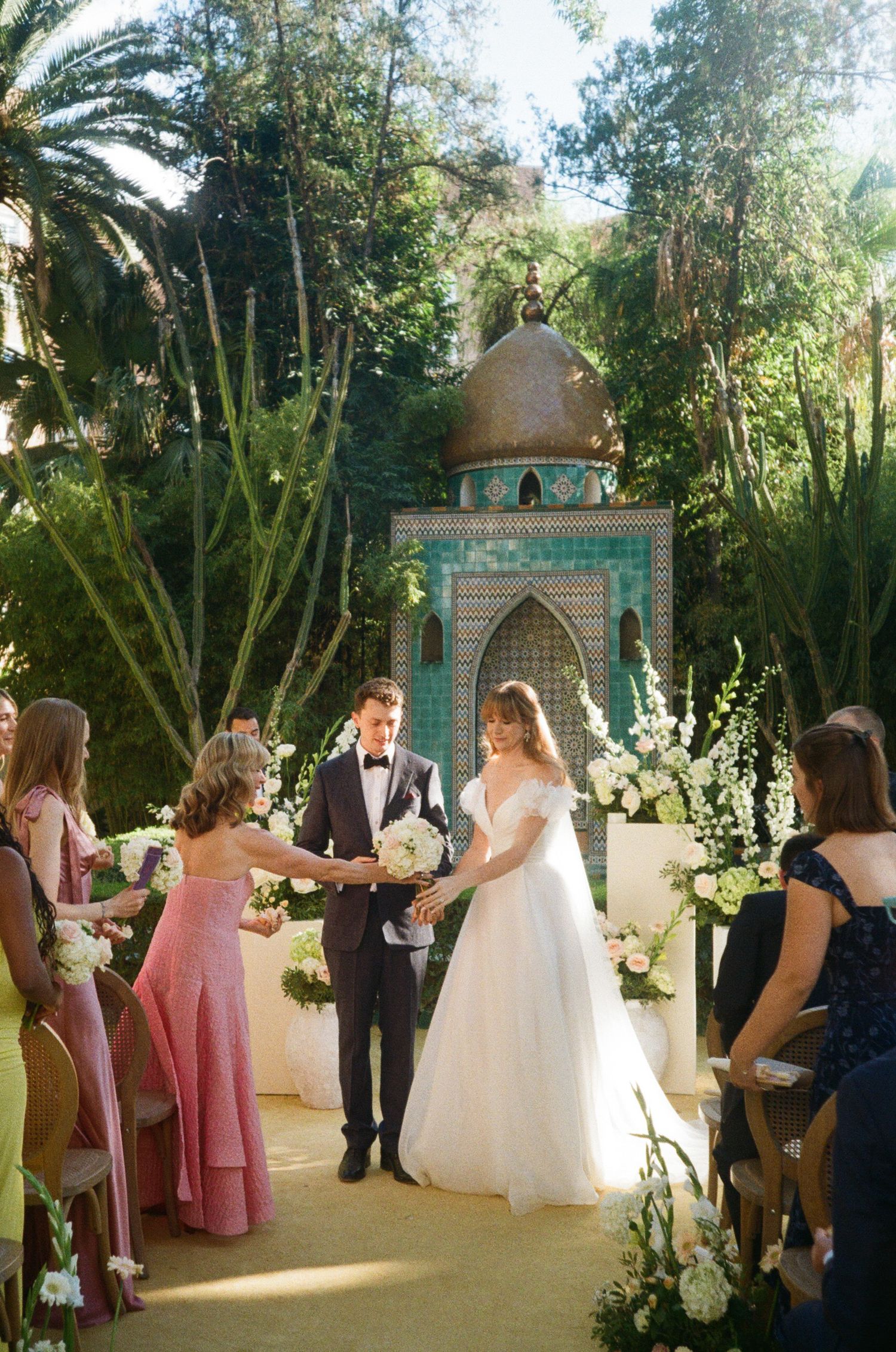 A wedding ceremony sequence shows a bridal party entering and gathering at a whimsical garden chapel with turquoise accents.