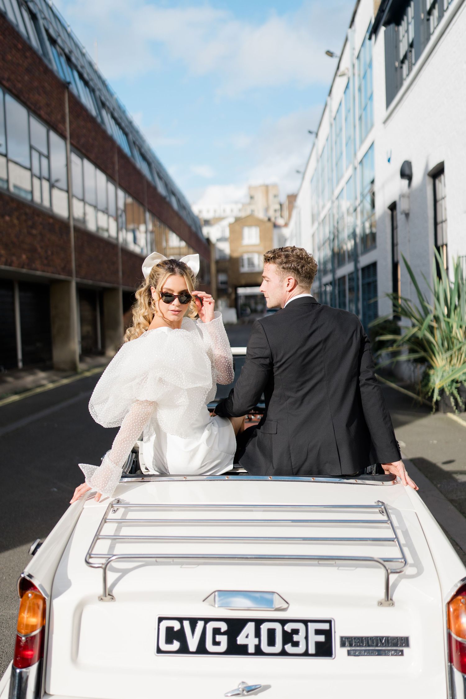 Couple sitting in white vintage convertible car on urban street.