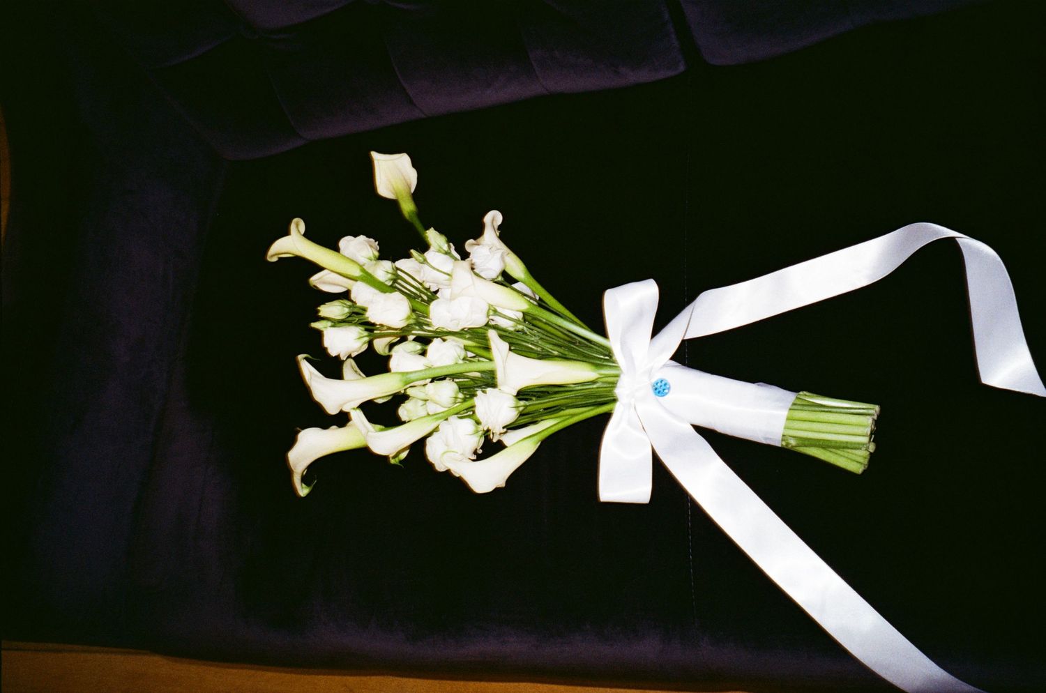 A simple white calla lily bouquet tied with a white satin ribbon against a dark background.