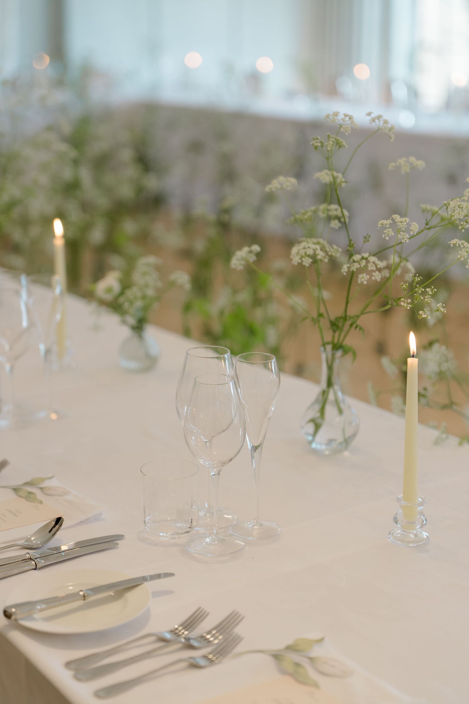Elegant wedding reception table set with crystal glasses, silver cutlery, candles and delicate wildflowers.