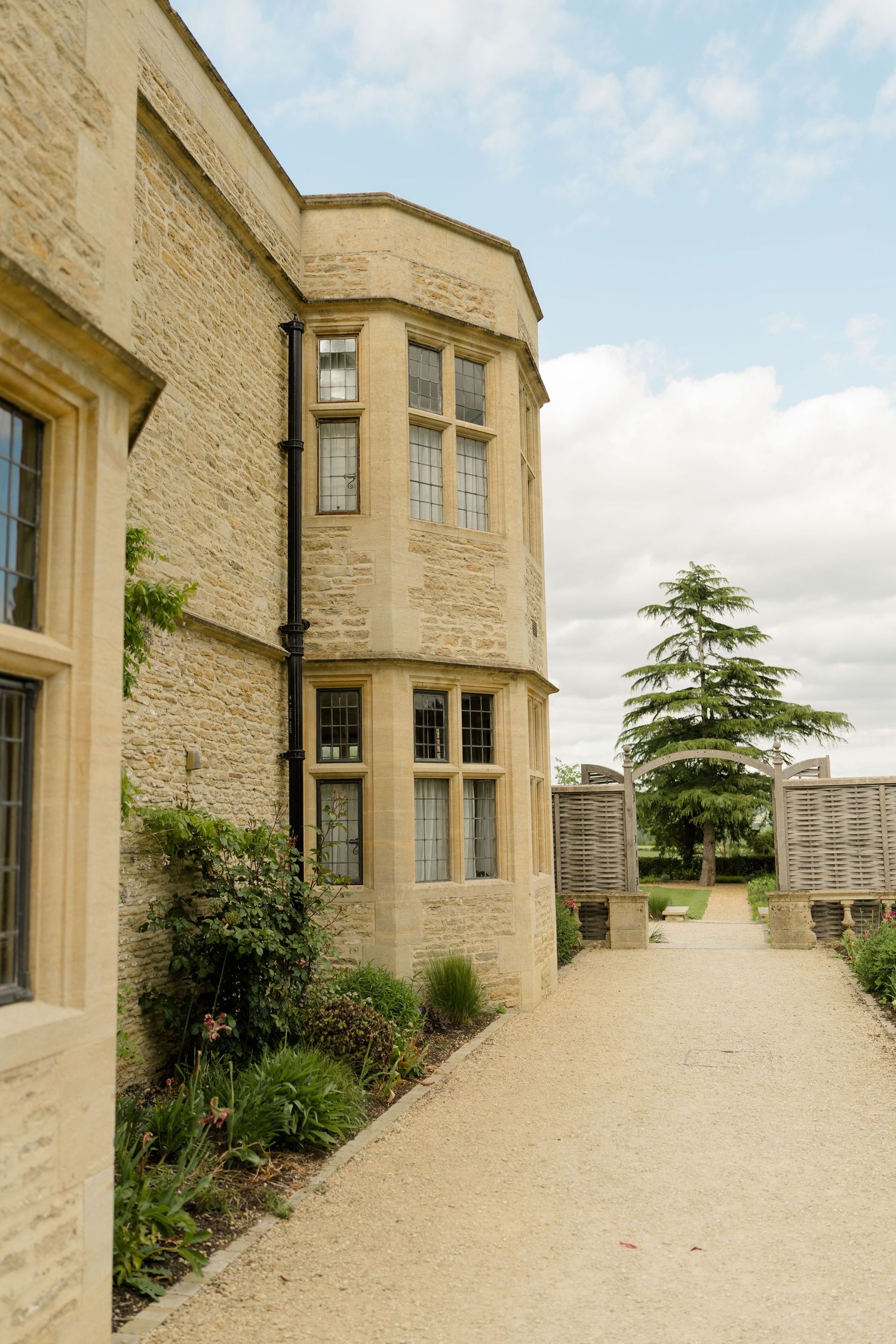 Stone manor house exterior with bay windows and gravel pathway leading to garden.