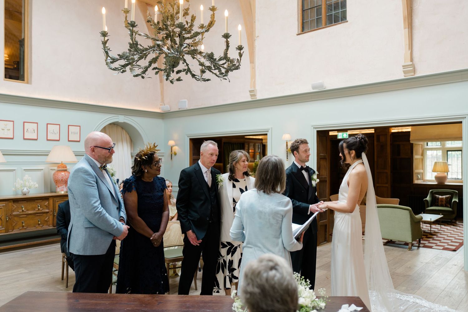 Elegant wedding ceremony indoors with couple exchanging vows before guests under a grand chandelier.