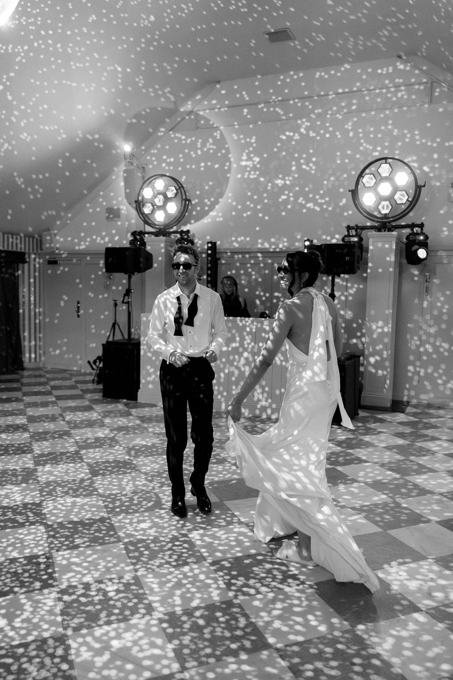 Black and white photo of a couple dancing under sparkling lights on a checkered wedding dance floor.