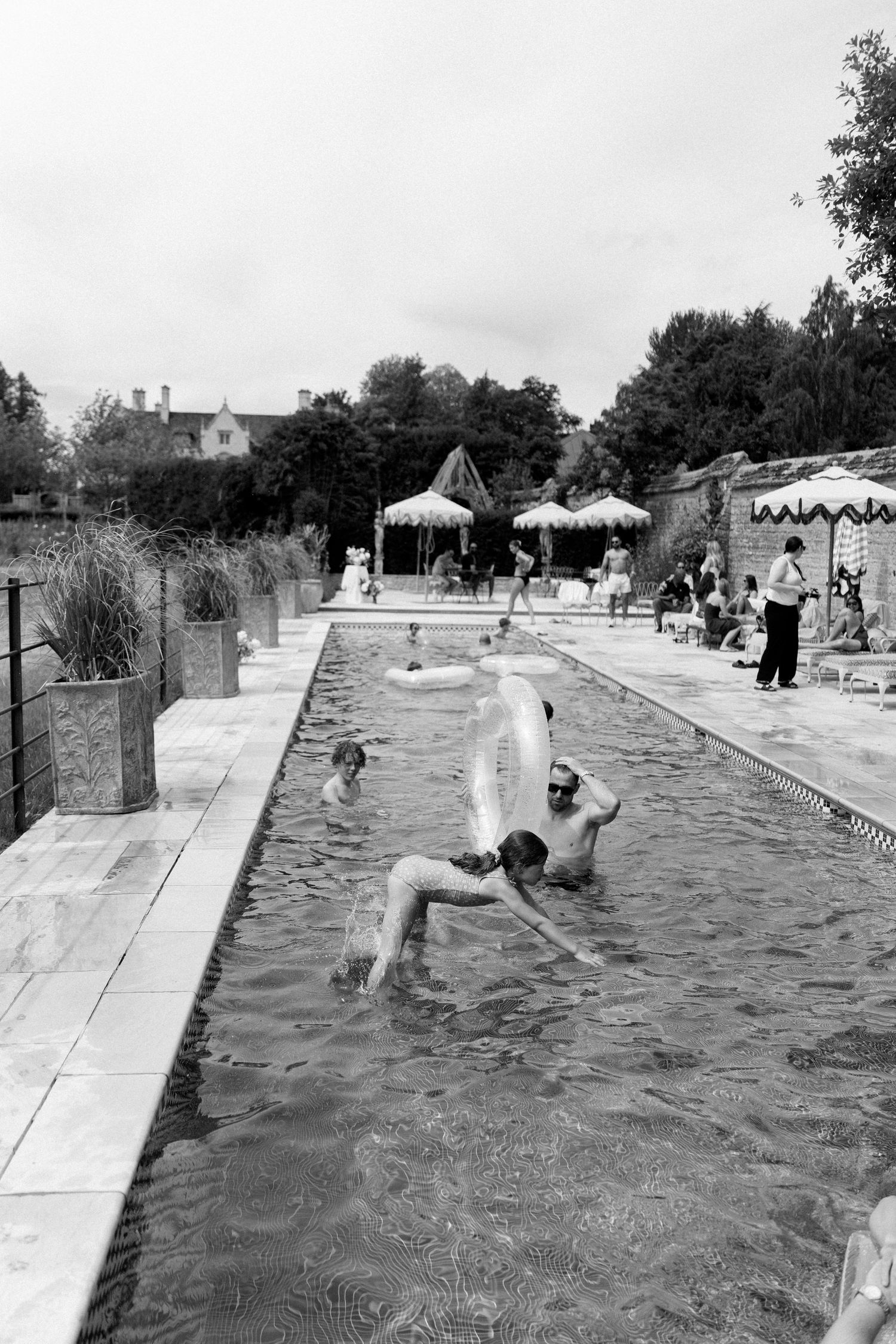Black and white photo of wedding guests swimming and playing with inflatables in outdoor pool.