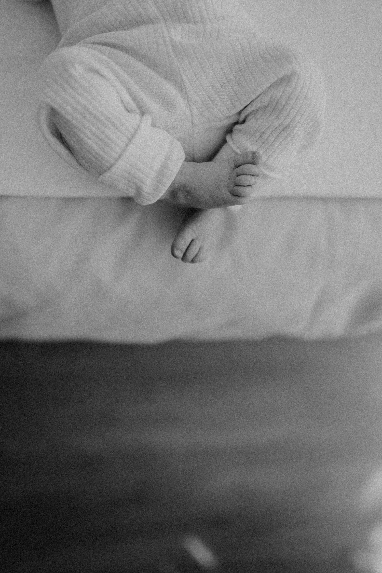 A sleeping infant in ribbed white clothing on light colored bedding.