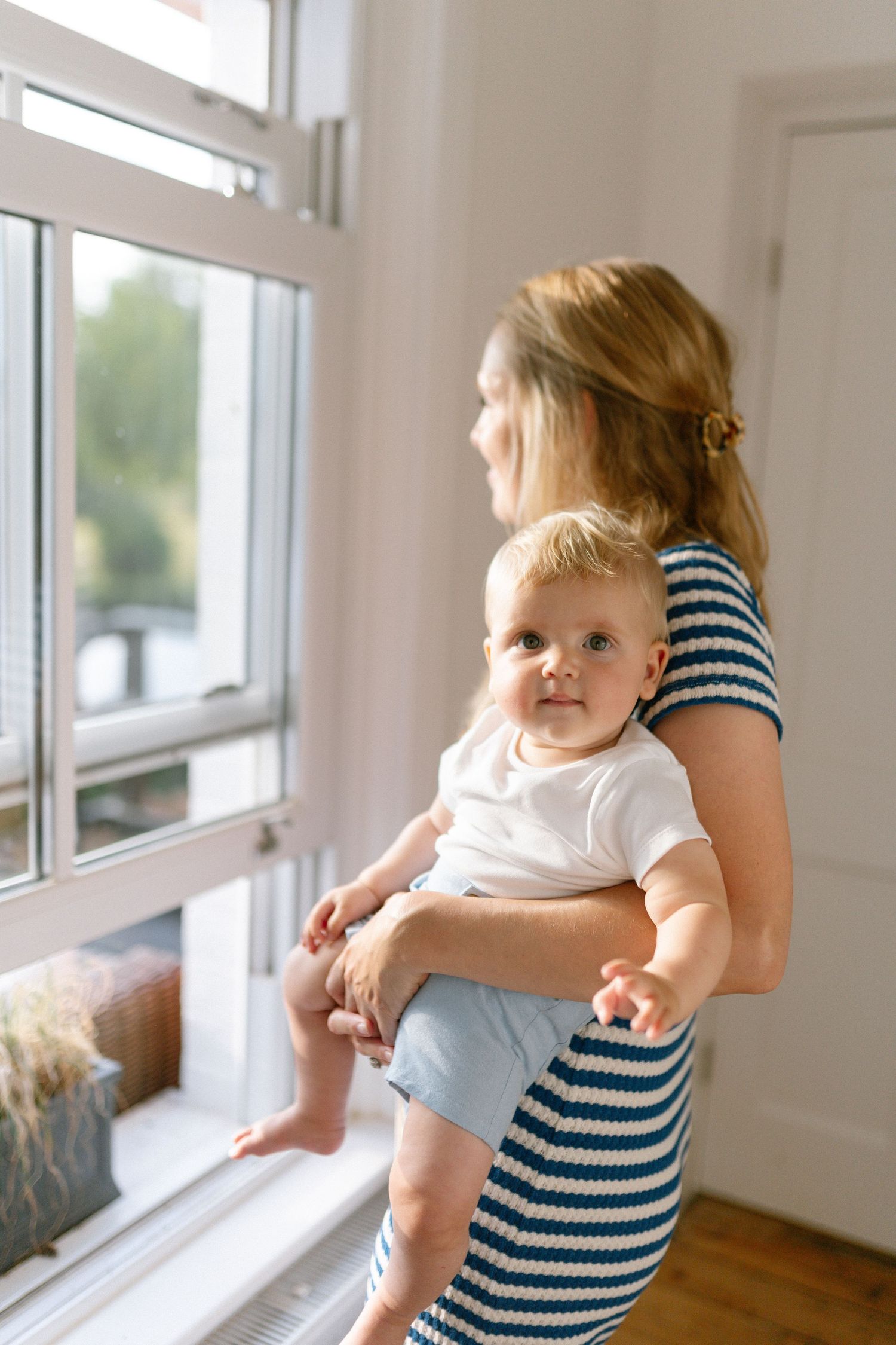 A tender moment by a bright window as a striped shirt-wearing figure holds a small child.