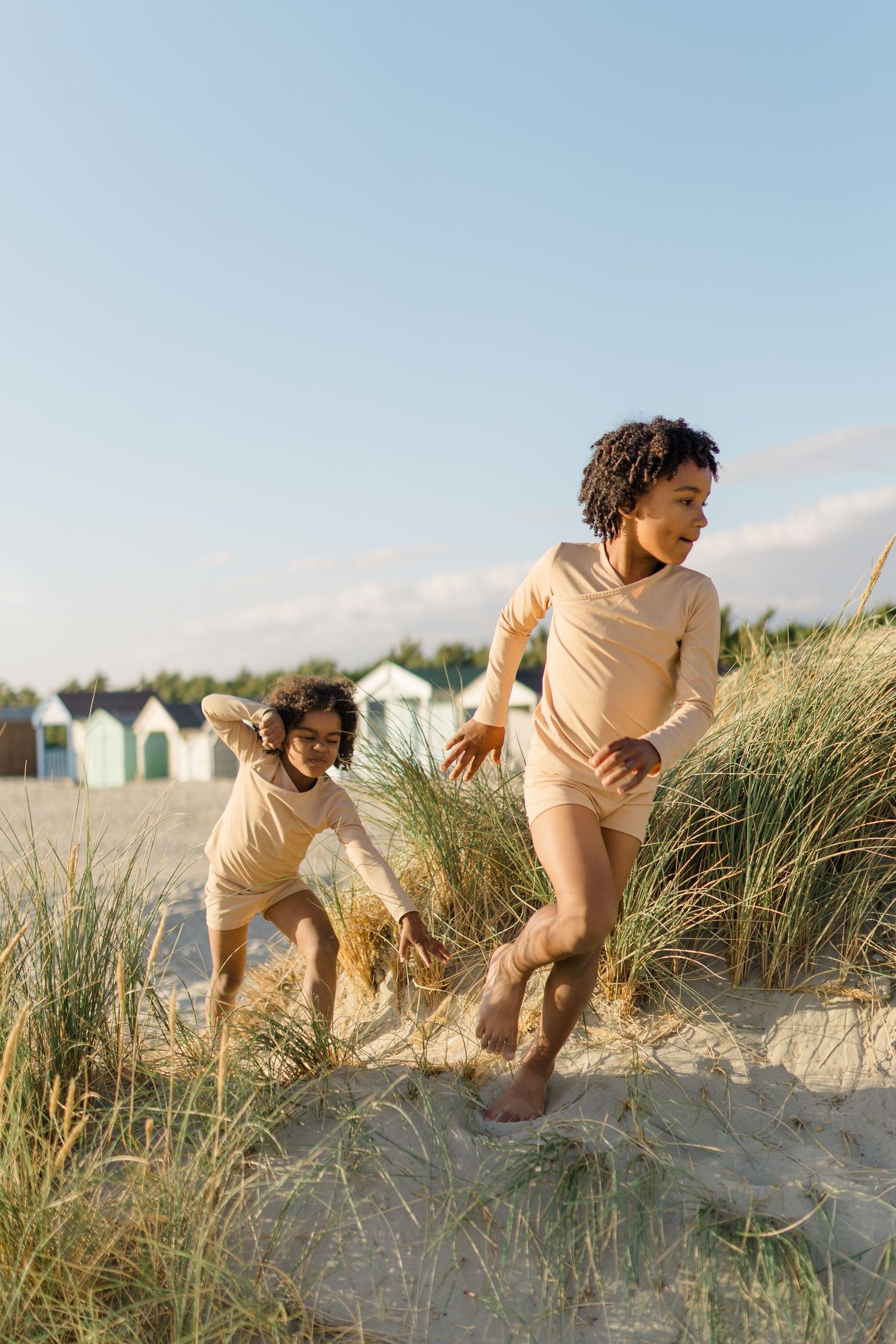 People climbing sand dunes with beach huts visible in background.