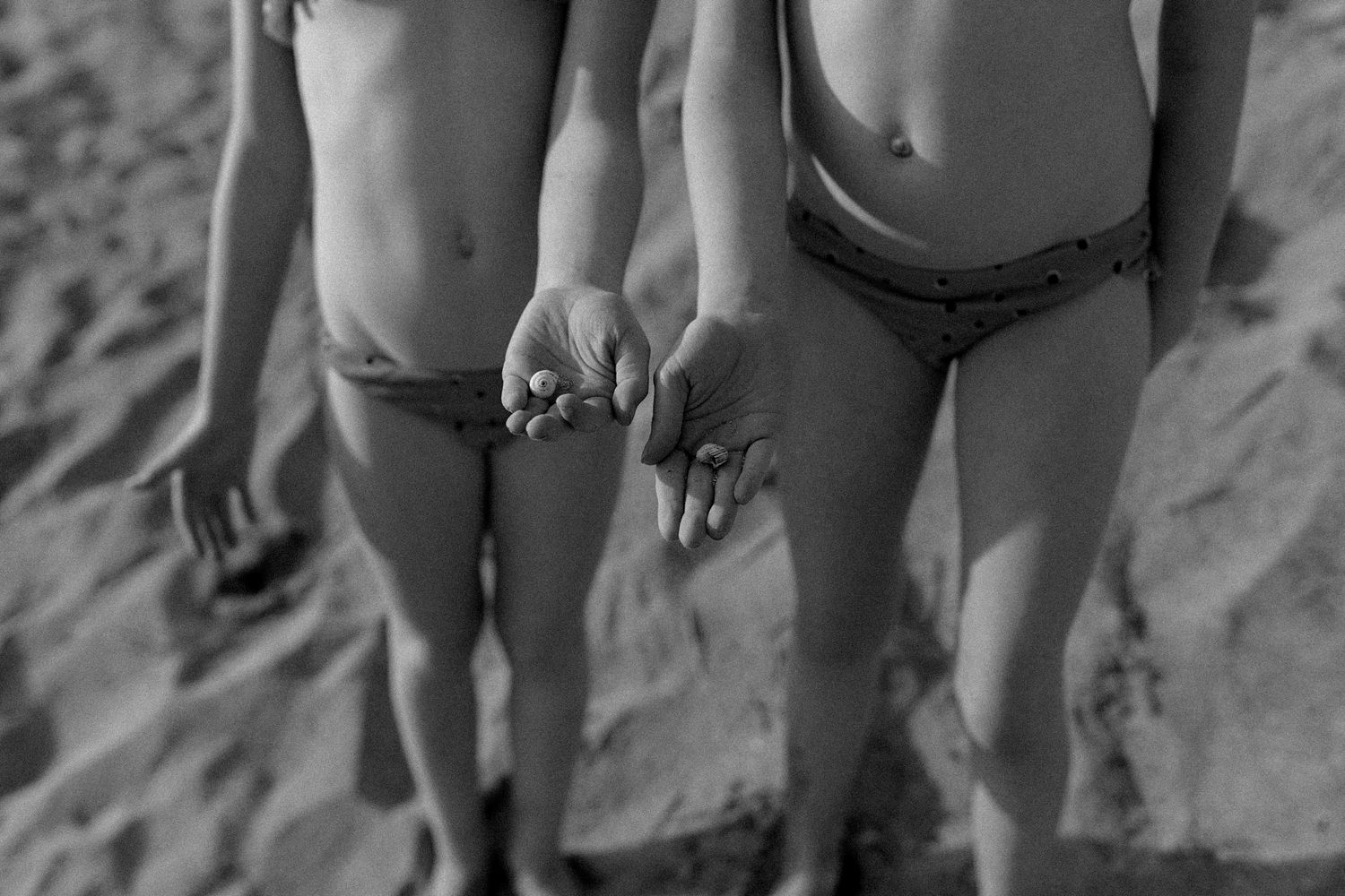 Close-up view of beachgoers' legs and feet standing in wet sand at the shoreline.