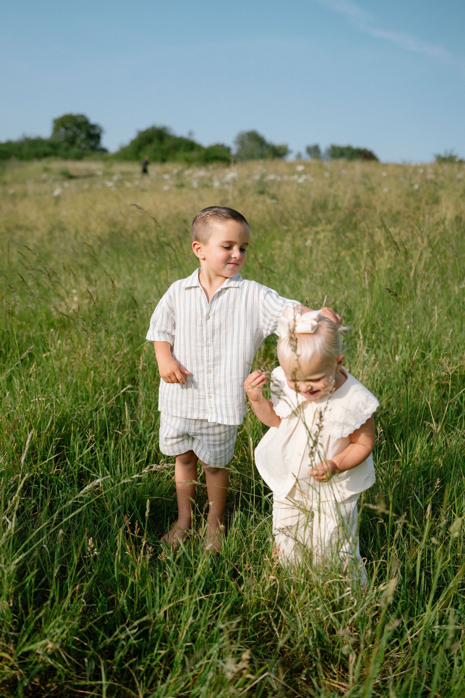 Two small children playing together in tall grass on a sunny summer day.