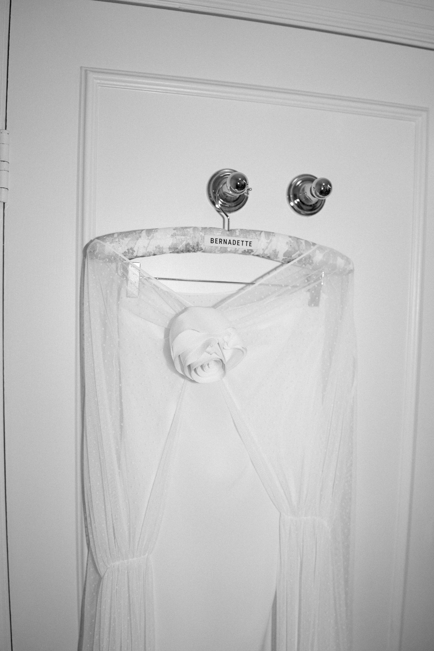 White wedding dress hanging on door hooks against light colored wall.