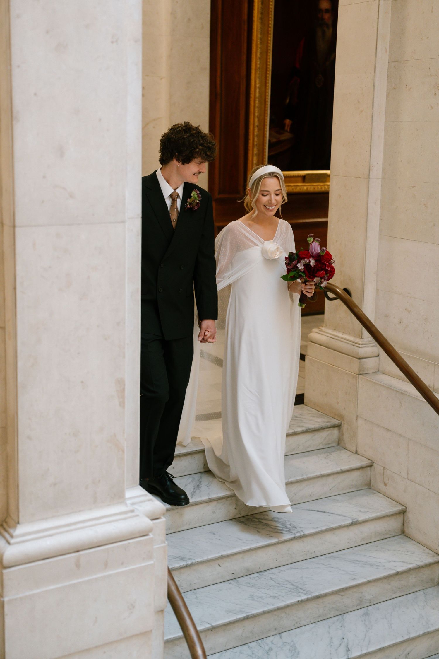 Wedding couple descending marble steps in an elegant building with classical architecture.