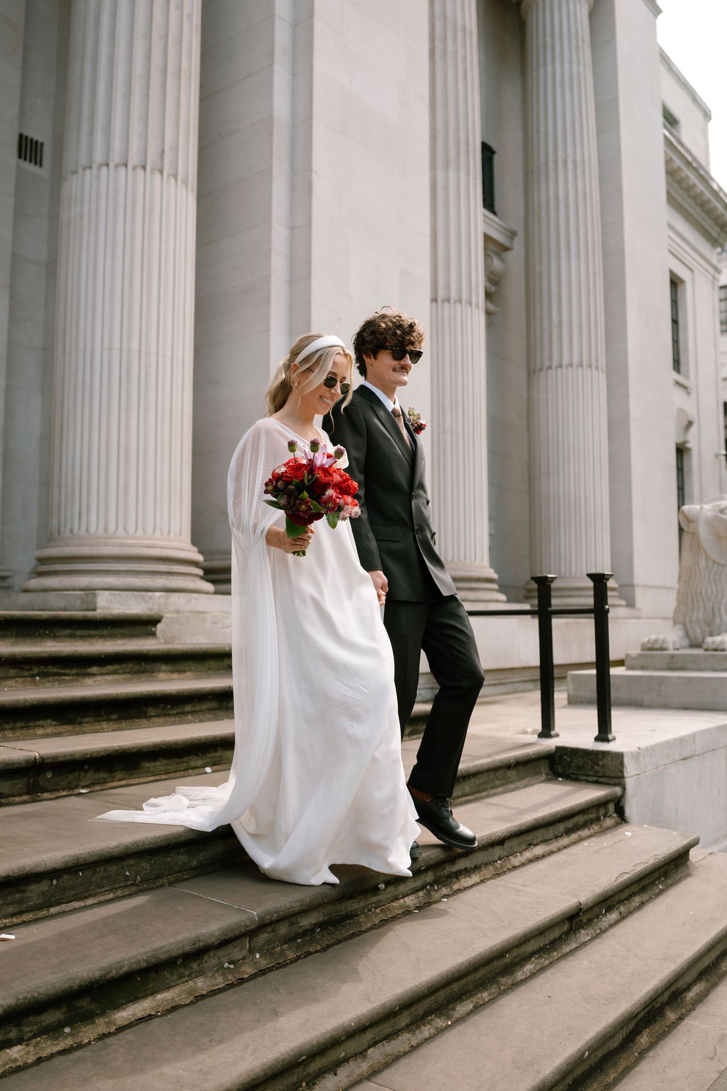 Wedding couple descending grand stone steps with classical columns in the background.