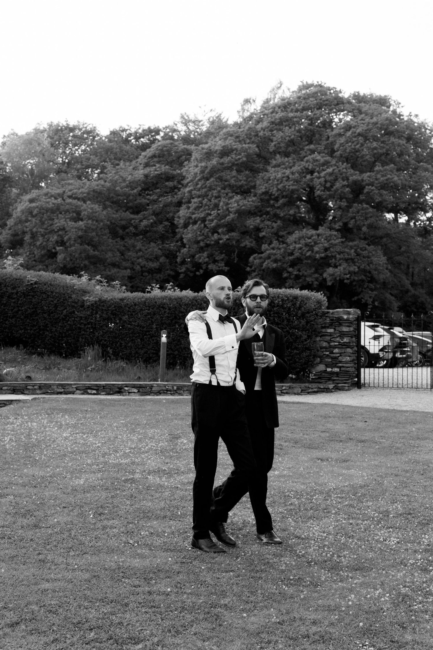 Wedding party members in formal attire stand on grass during outdoor event.