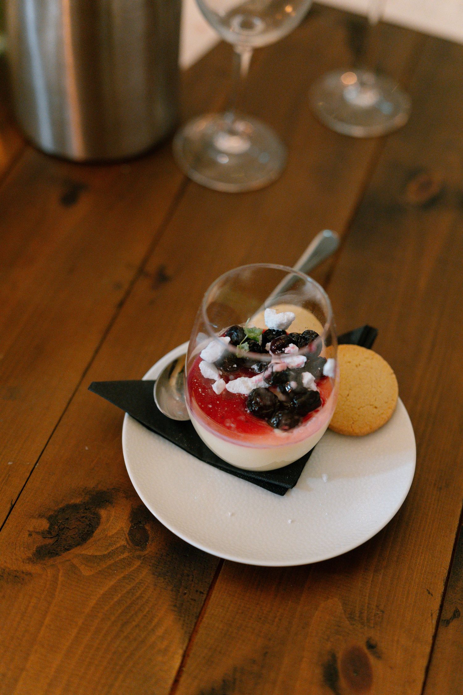 Elegant dessert plate with red and white cream garnished with dark berries on wooden table.